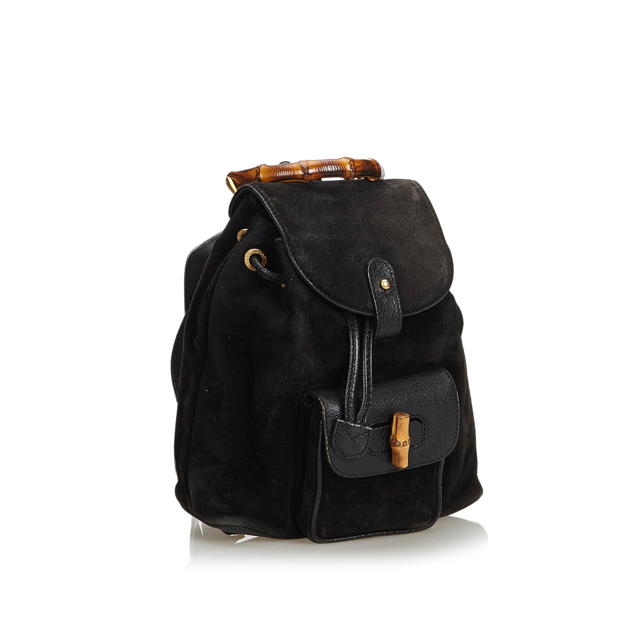 This backpack features a suede body, an exterior flap pocket with bamboo twist lock closure, flat leather back straps, a bamboo top handle, a top flap with a button closure, a top drawstring closure, and an interior zip pocket. It carries as B+
