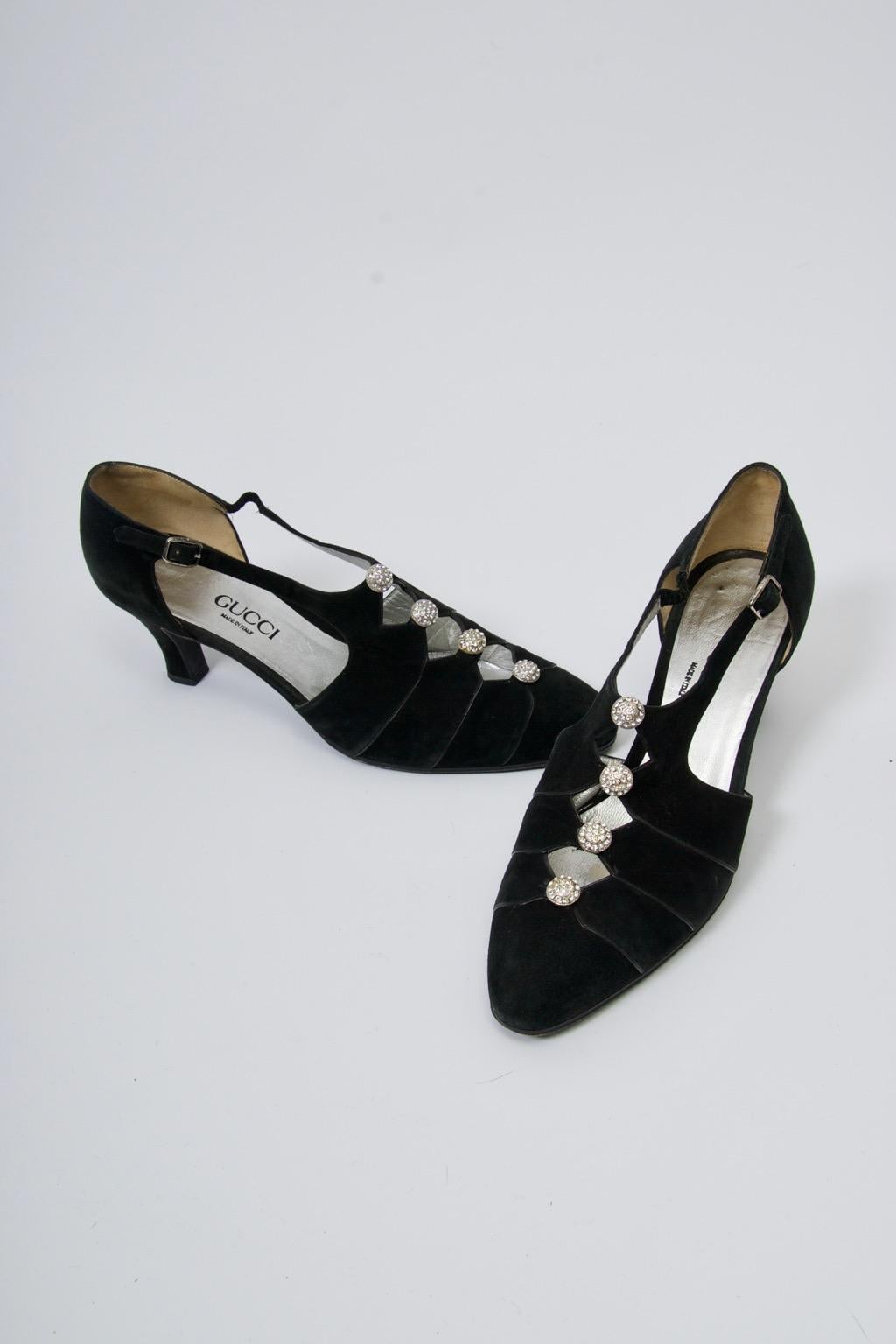 Vintage Gucci evening shoes in black suede adorned with round rhinestone buttons at the cut-our T-strap form. Narrow black leather border edging. Low heel provides a level of comfort to these elegant shoes. Approximate size 7.