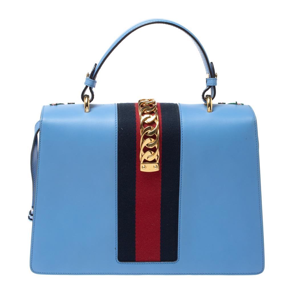 From the house of Gucci comes this gorgeous Sylvie bag that will perfectly complement all your outfits. It has been luxuriously crafted from blue leather and styled with floral embroidery on the front, chain-web decorated flap, and a buckle lock