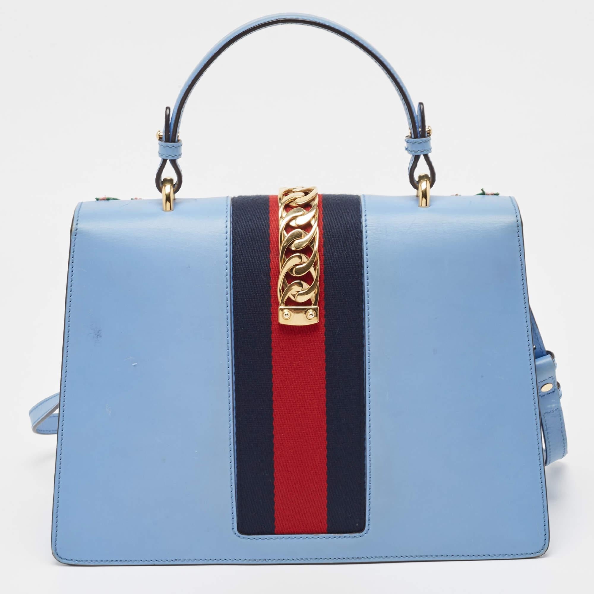 La maison Gucci nous offre ce magnifique sac Sylvie qui s'harmonisera parfaitement avec toutes vos tenues. Il a été luxueusement confectionné en cuir bleu et présente une broderie florale sur le devant, un rabat décoré d'une toile de chaîne et une