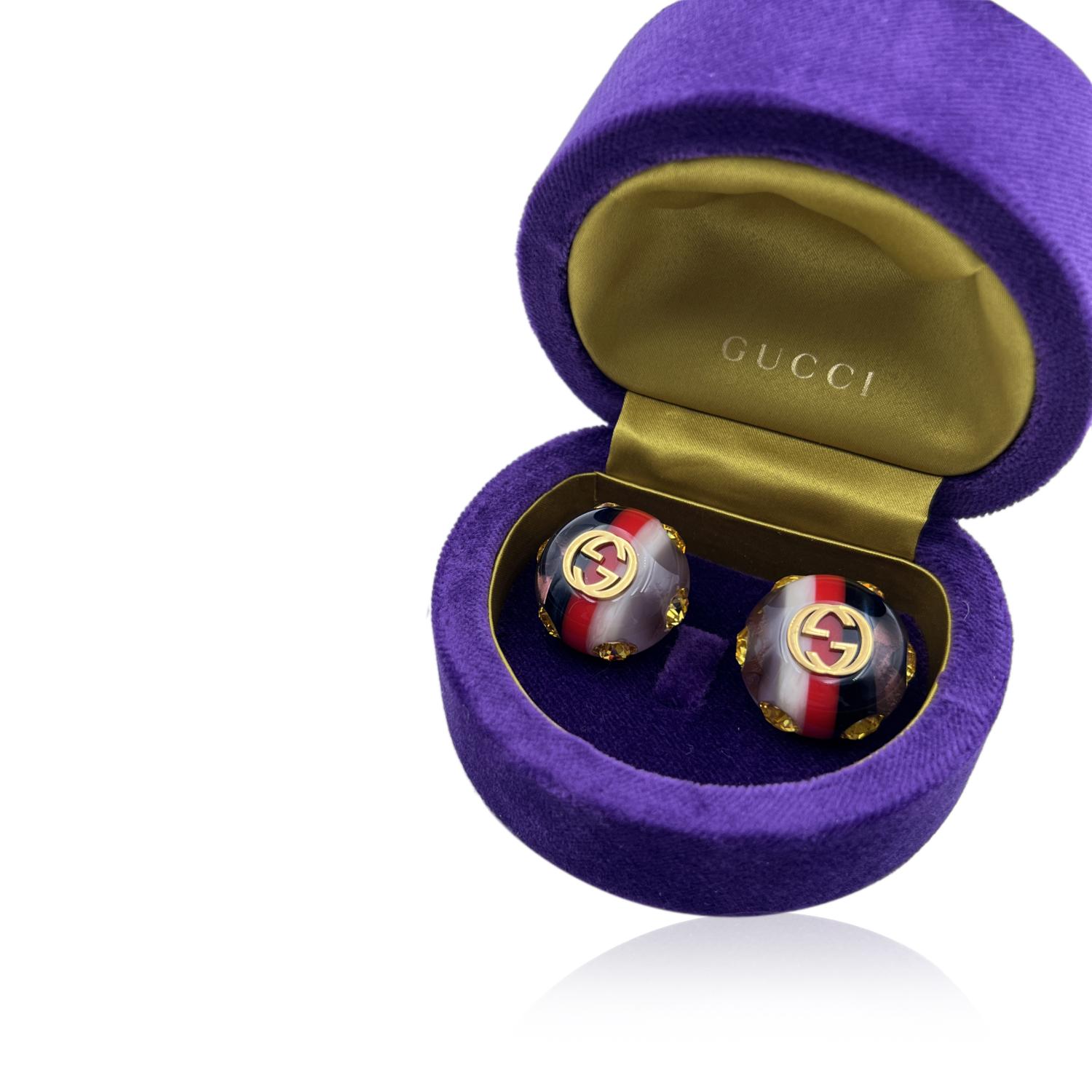 Beautiful GUCCI Resin Web Stud Pin earrings. They feature clear, white, red and blue stripes and yellow crystals emebllishment. For pierced ears. Gold metal GG logo on the front. 'Gucci - Made in Italy' engraved on the reverse of each earring.