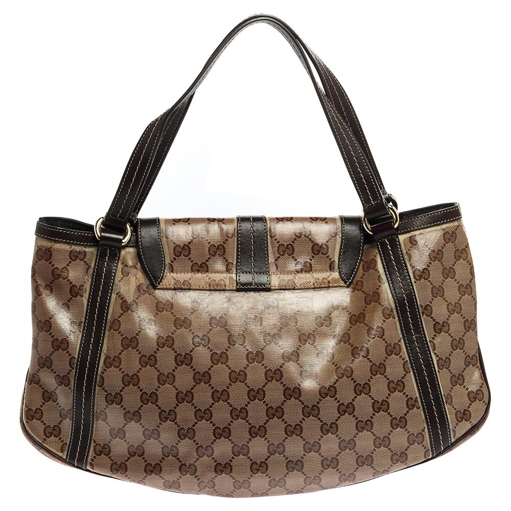 Made from GG crystal canvas and brown leather in a graceful design, this Gucci bag is a wardrobe essential. It features a flap adorned with gold-tone bows and dangling brand-accented details. The spacious fabric interior ensures enough space for