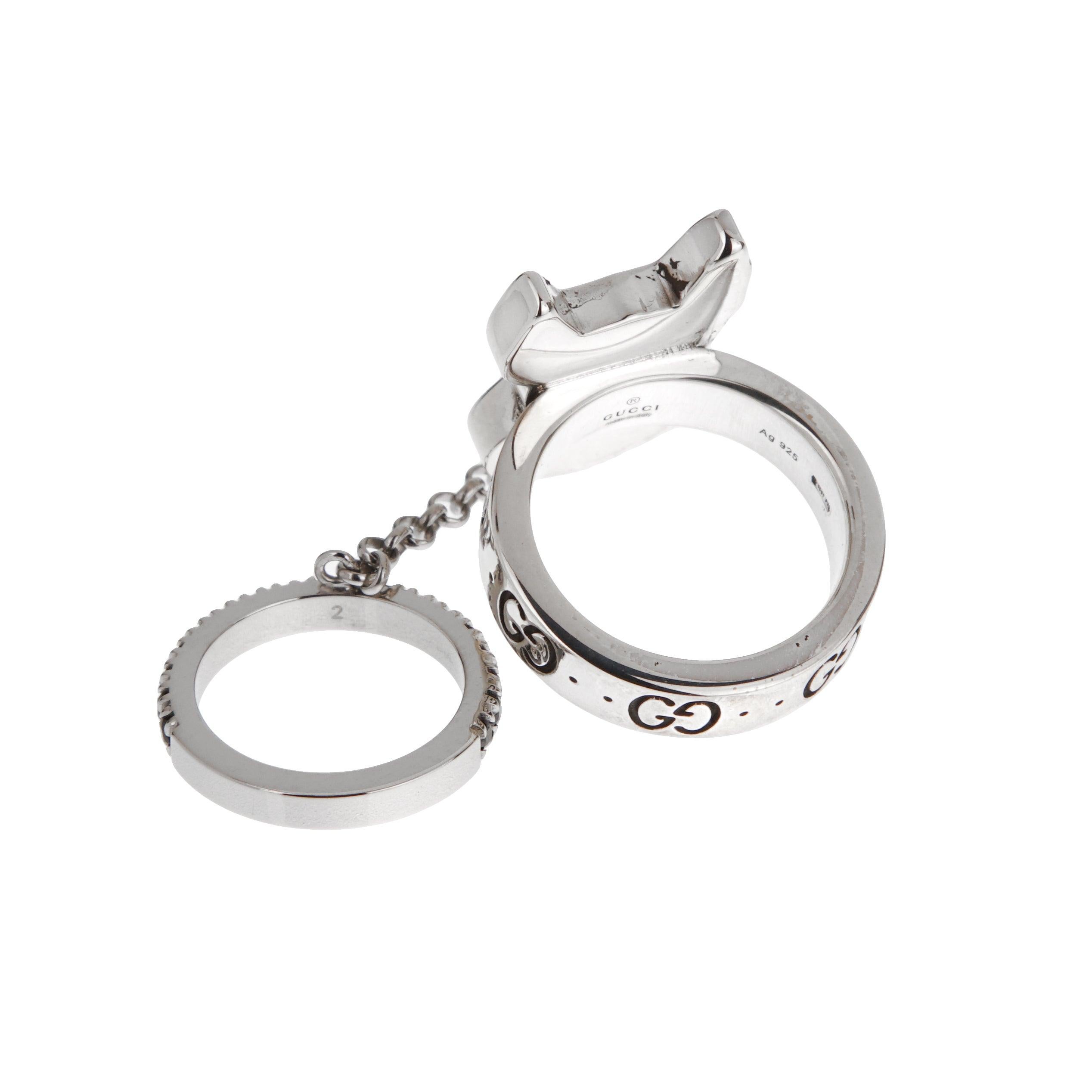 Un anillo doble Gucci, elaborado en plata de ley. Presenta un retrato esmaltado de Bosco, la mascota del Boston Terrier, en la anilla superior. Una cadena de plata de ley se conecta a una banda inferior adornada con espinelas negras, mostrando un