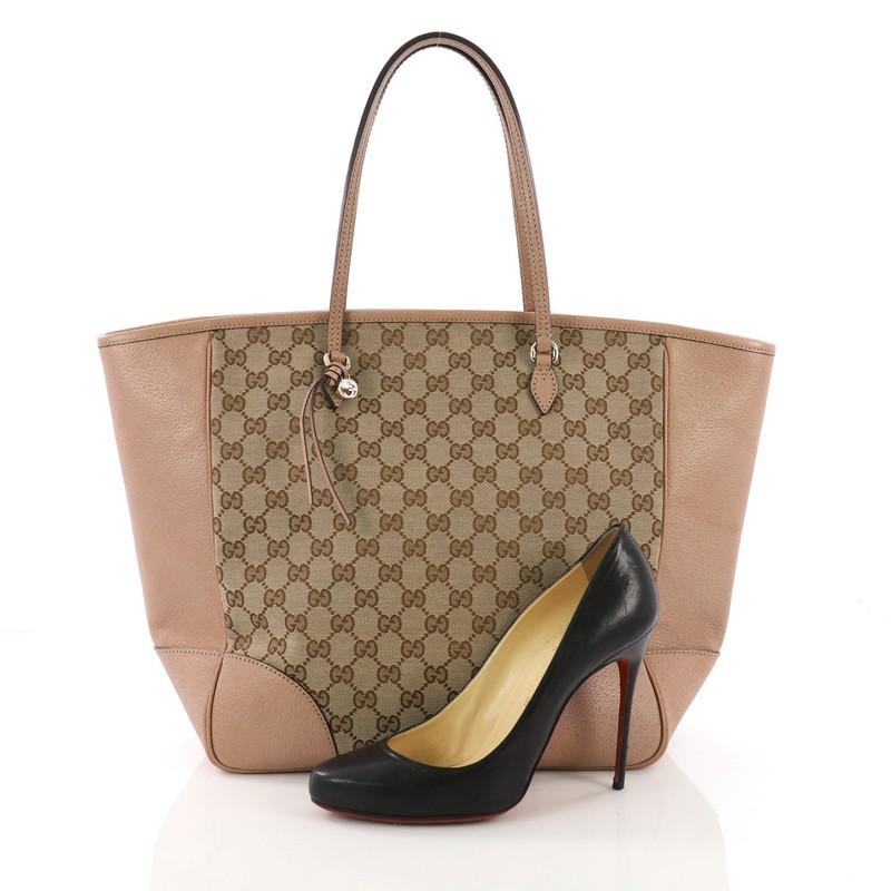 This Gucci Bree Tote GG Canvas Medium, crafted from brown GG canvas with mauve leather, features dual tall handles and gold-tone hardware. Its top zip closure opens to a beige fabric interior with side zip and slip pockets. **Note: Shoe photographed