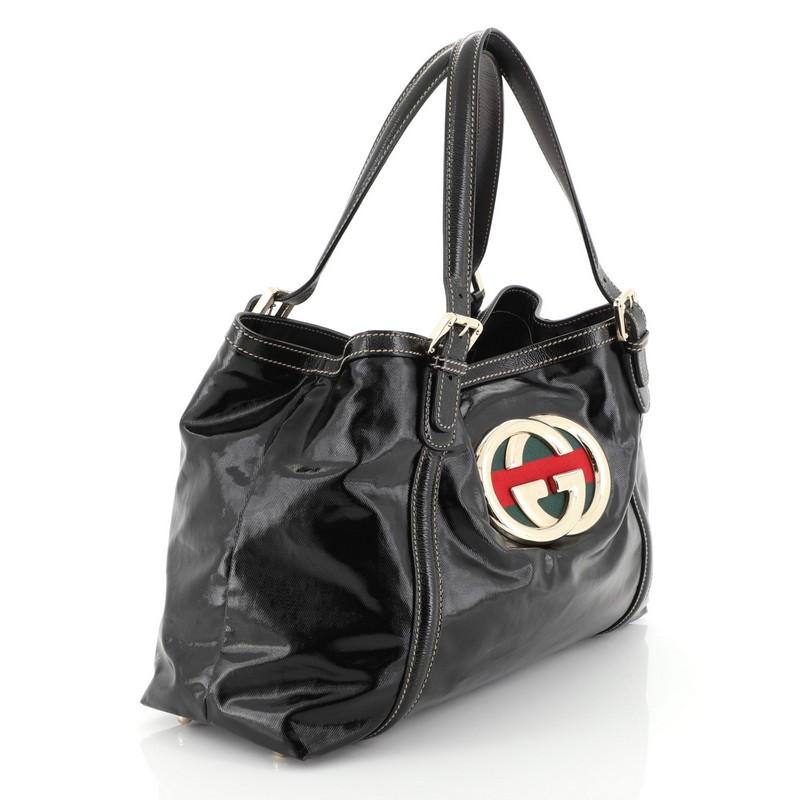 This Gucci Britt Web Tote Dialux Coated Canvas Medium, crafted in black dialux coated canvas, features interlocking GG metal logo with signature web fabric design, dual top handles with buckle strap details and gold-tone hardware. Its magnetic snap