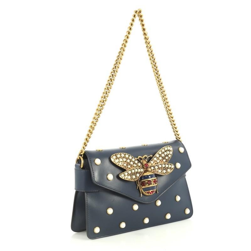 This Gucci Broadway Pearly Bee Shoulder Bag Embellished Leather Mini, crafted from blue leather, features chain link strap, multiple pearl studs, metal bee design, and aged-gold tone hardware. Its magnetic snap closure opens to a neutral leather