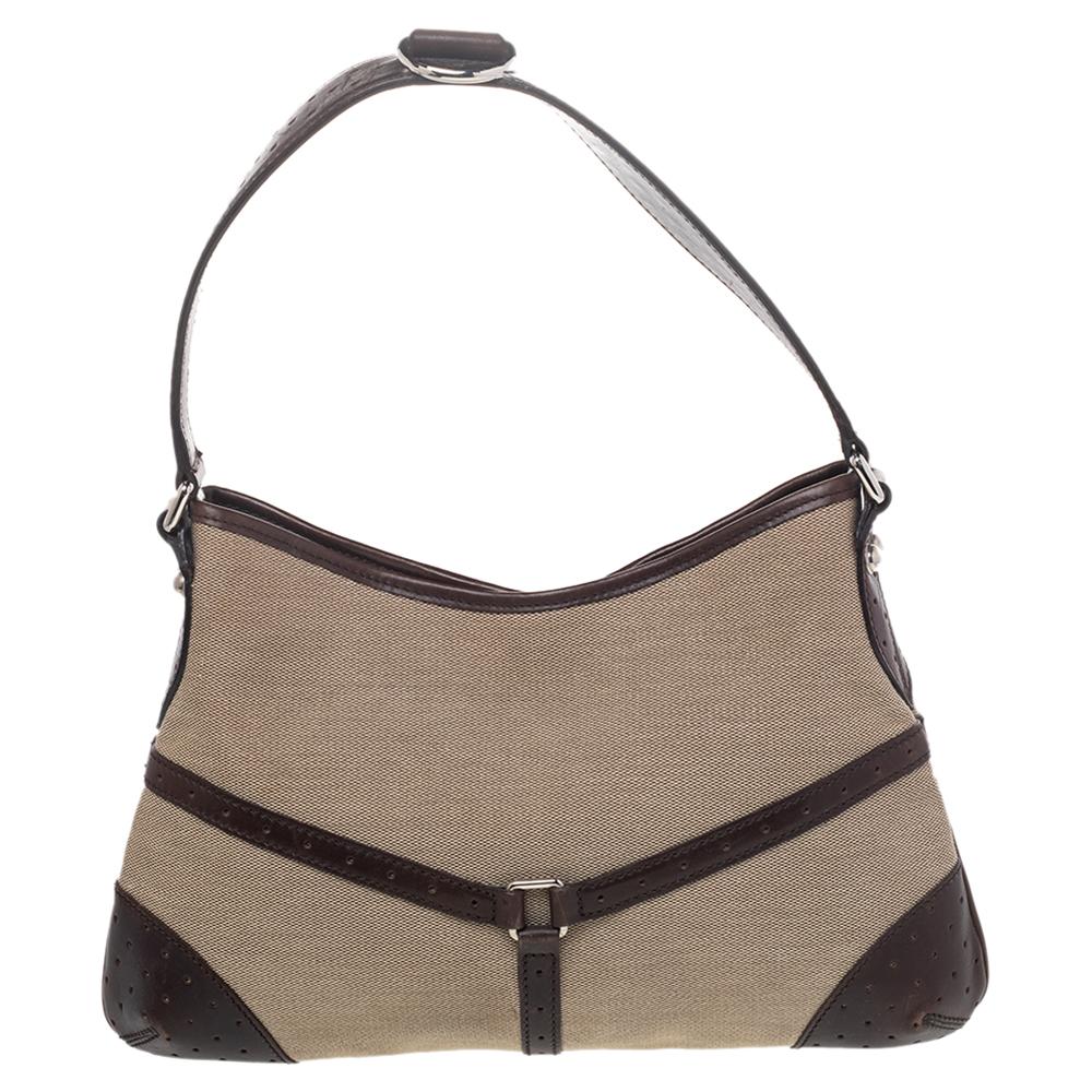 This Gucci hobo will conveniently hold all your essentials in great style. Fashioned in beige canvas and brown perforated leather, this classy bag comes with a top zip closure and the GG logo over the signature Web trim on the front. This hobo is