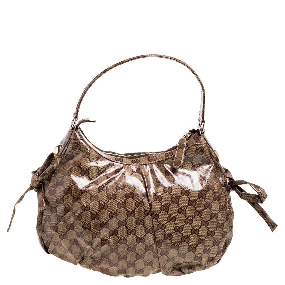 This hobo from the house of Gucci can work well for any occasion. The bag is crafted from the signature GG crystal canvas and is enhanced with the Web stripe on the front. It flaunts a ring accent along with a logo detailed charm and dual bows on