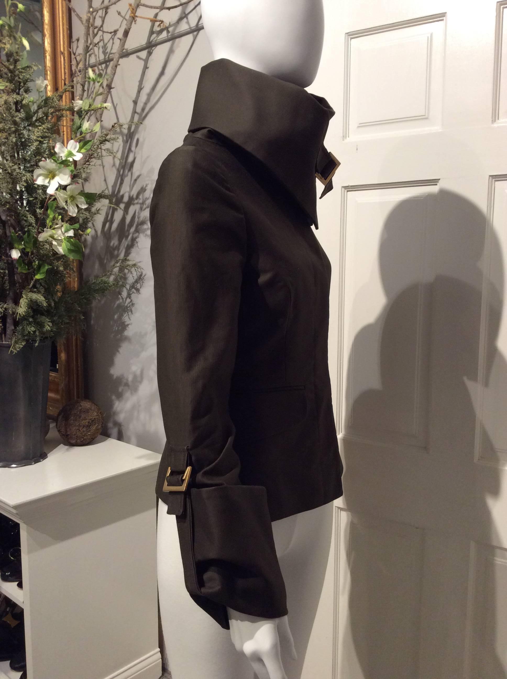 Gucci hip length dark brown, fitted, military inspired fjacket with fold over high collar and cuffs. The collar and cuffs are each kept in place by a single brushed gold buckle. The jacket closes with four hidden buttons and has two flap front