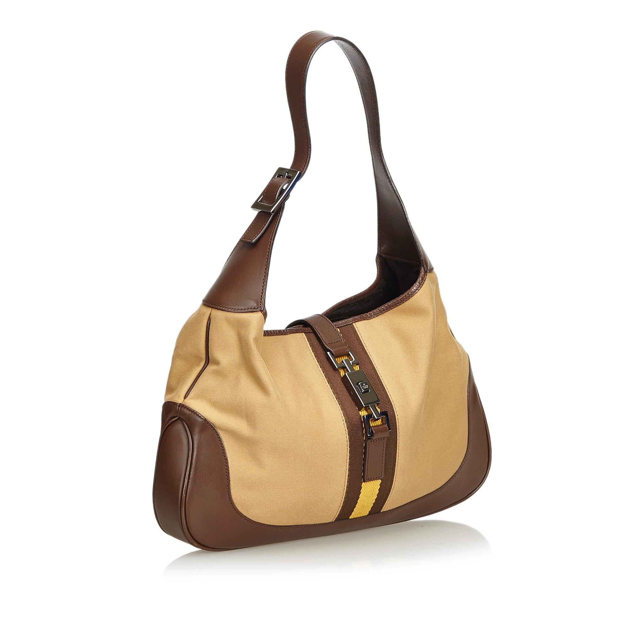 The Jackie shoulder bag features a canvas body with leather trim, a flat leather strap, open top with flat strap and push lock closure, and interior zip pocket. It carries as AB condition rating.

Inclusions: 
Dust Bag

Dimensions:
Length: 21.00