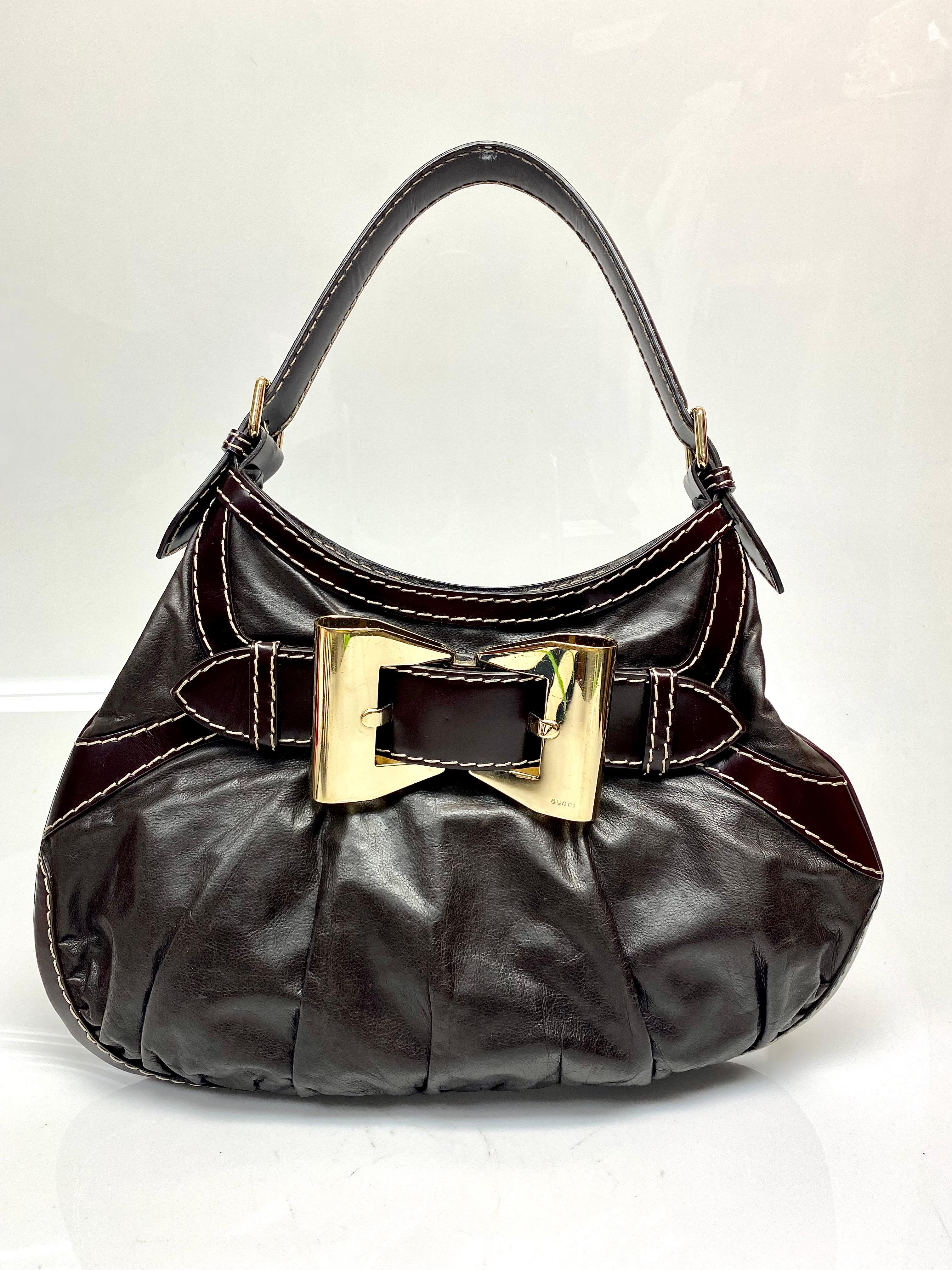 Gucci Brown Leather Gold Hardware Handbag. This beautifully made Gucci handbag is perfect for any season. The bag features a gold hardware bow front, white stitched lining and one interior zipped pocket. Item is in good condition with some scuffs on