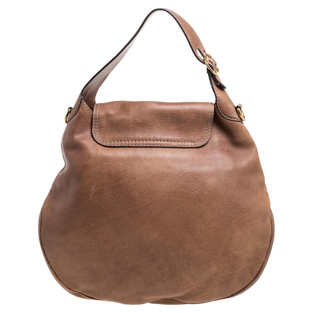 This gorgeous Gucci handbag is a throwback on the rugged, rustic Western look. The detachable braided shoulder strap and horse-bit details add to the vintage look of the brown leather. The fabric lining has one zippered pocket while an exterior