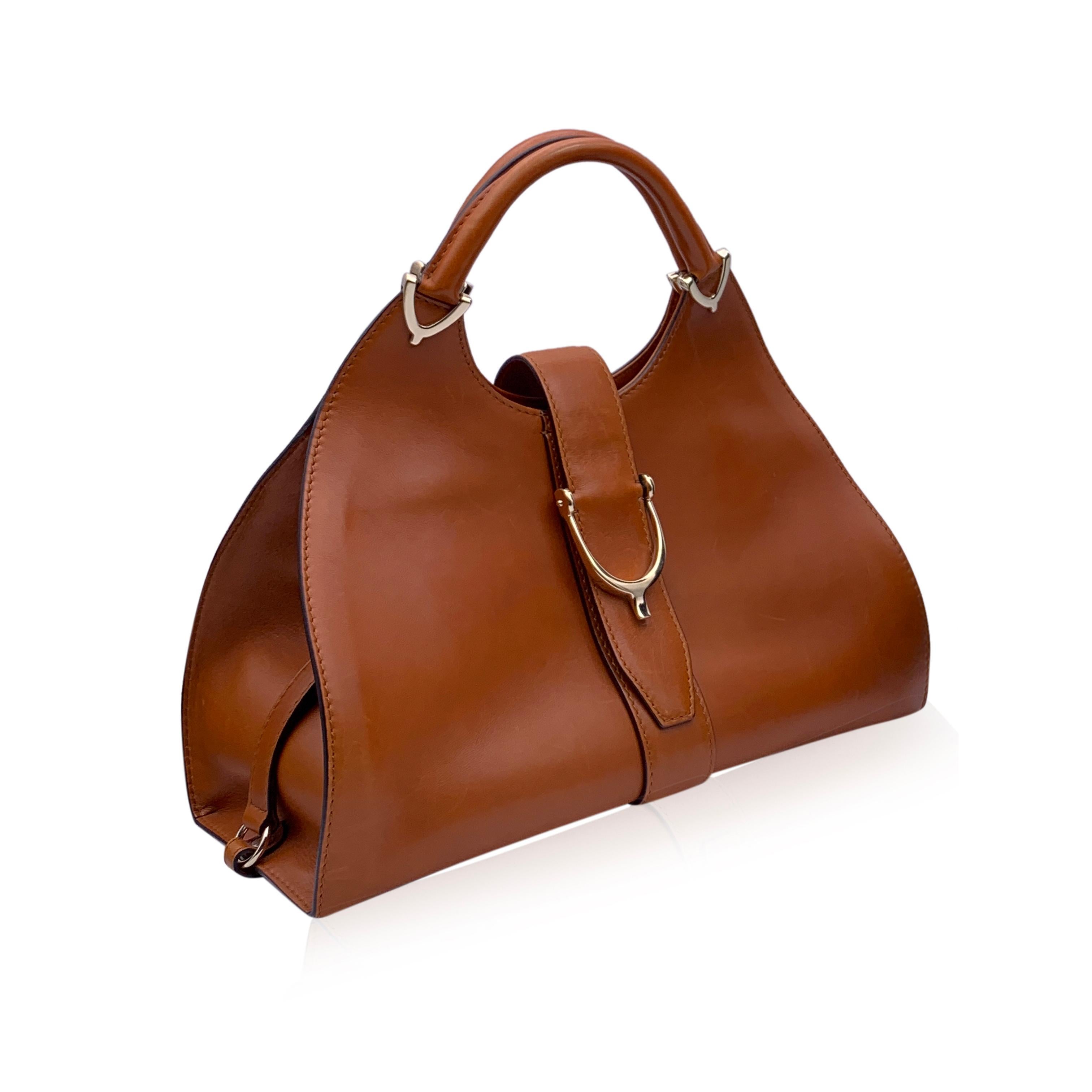 Beautiful Gucci 'Stirrup' hobo bag, crafted in brown leather. Light gold hardware. Fold over strap with button closure. Spur detailing on the front and on the handles. Canvas interior with 1 side zip pocket inside and 2 side open pockets. 'Gucci