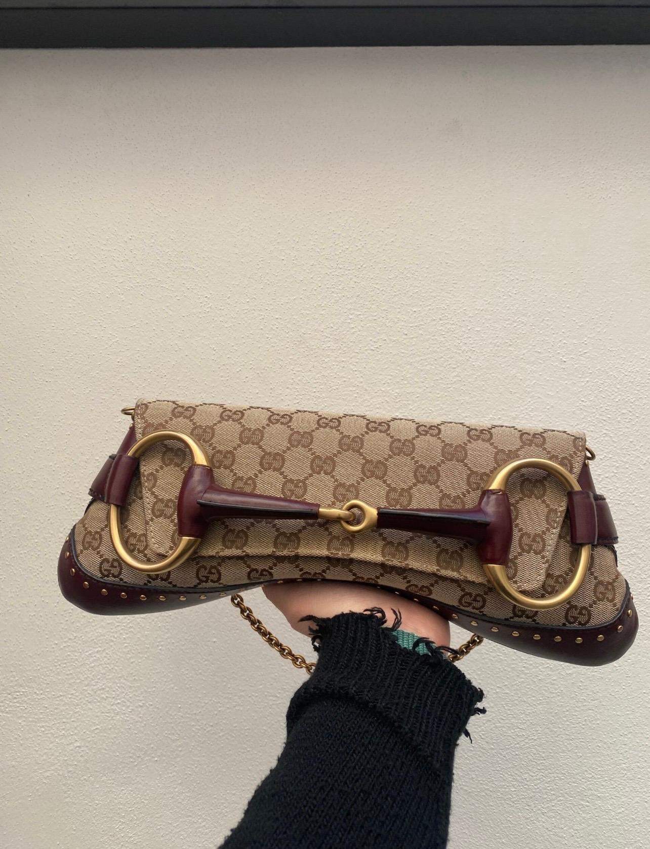 Gucci Tom Ford edition bag in GG Supreme canvas and burgundy leather with gold hardware.  Features a front flap with button closure. The interior is lined with a soft dark brown fabric.  The bag is equipped with a removable golden chain shoulder