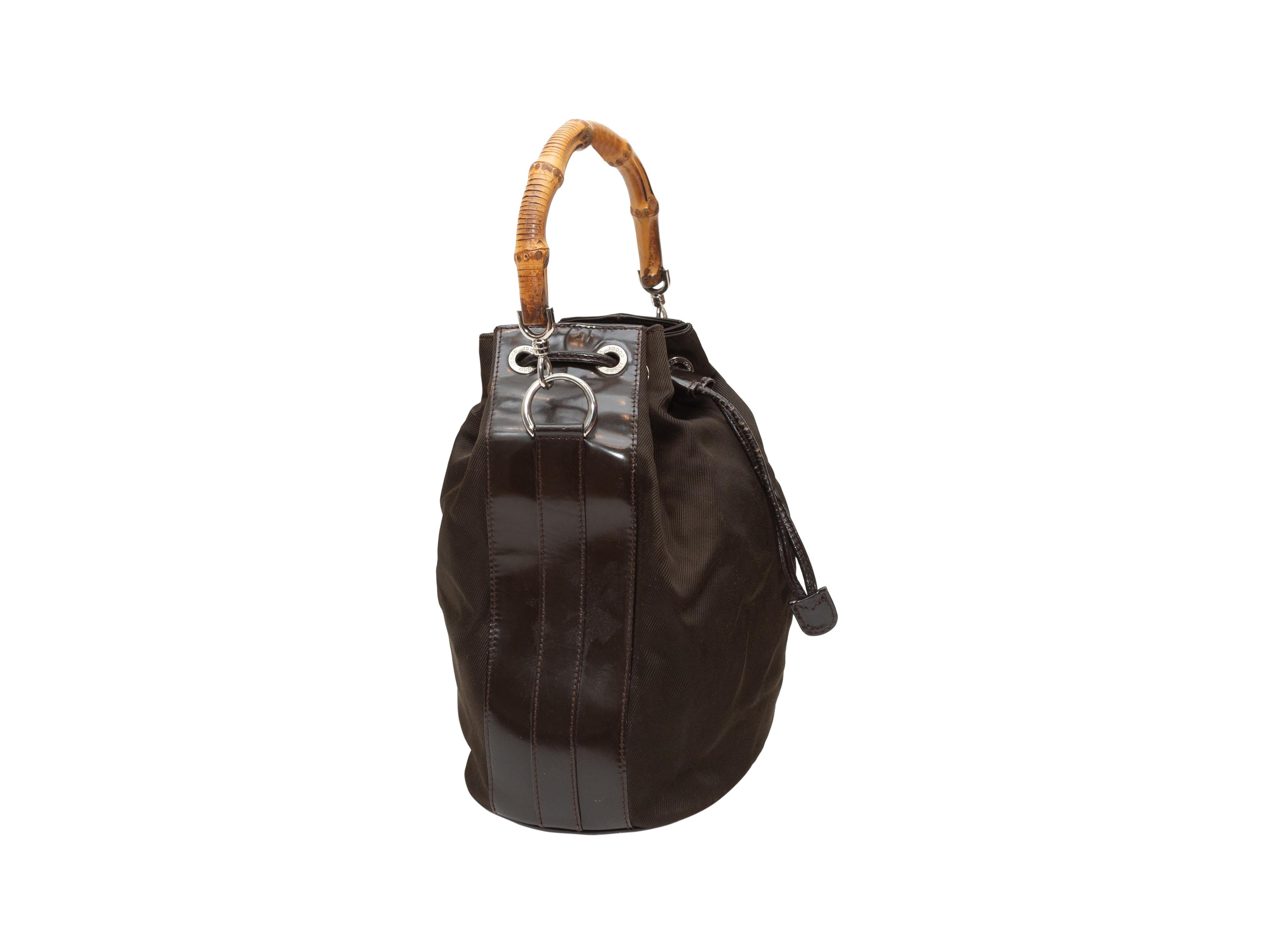 Product details: Vintage brown nylon bucket bag by Gucci. Leather trim throughout. Silver-tone hardware. Bamboo top handle. Optional shoulder strap. Drawstring closure at top. 10