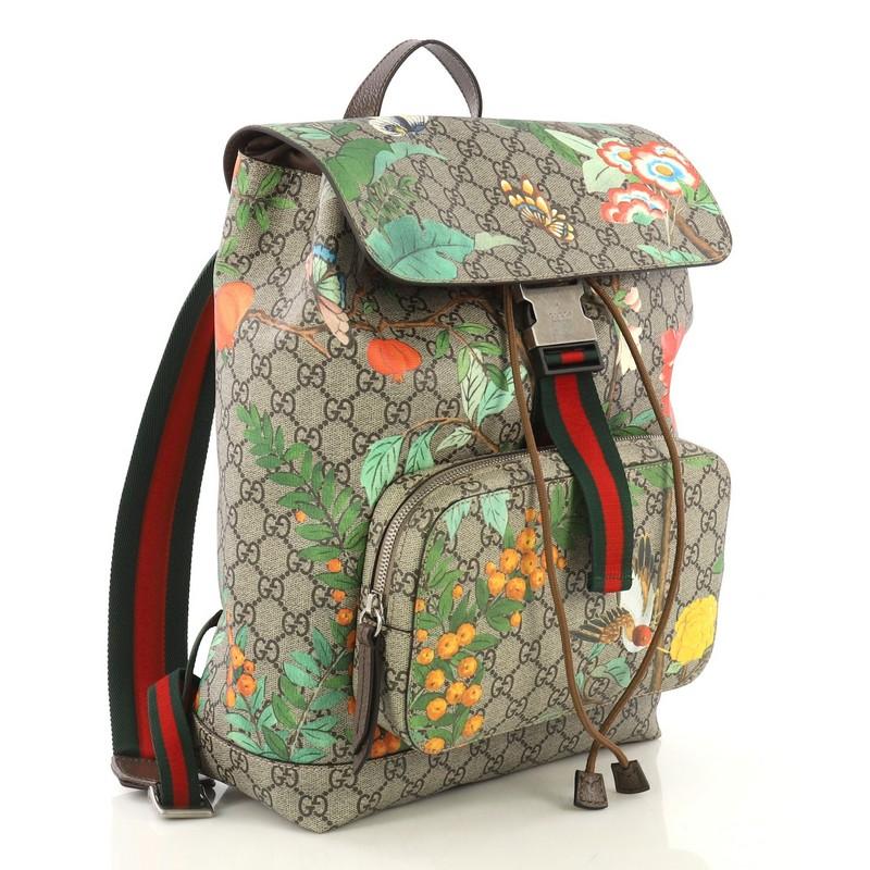 This Gucci Buckle Backpack Tian Print GG Coated Canvas Medium, crafted from brown GG supreme coated canvas overlaid with the Gucci Tian print, features adjustable padded nylon shoulder straps, exterior front zip pocket, and silver-tone hardware. Its