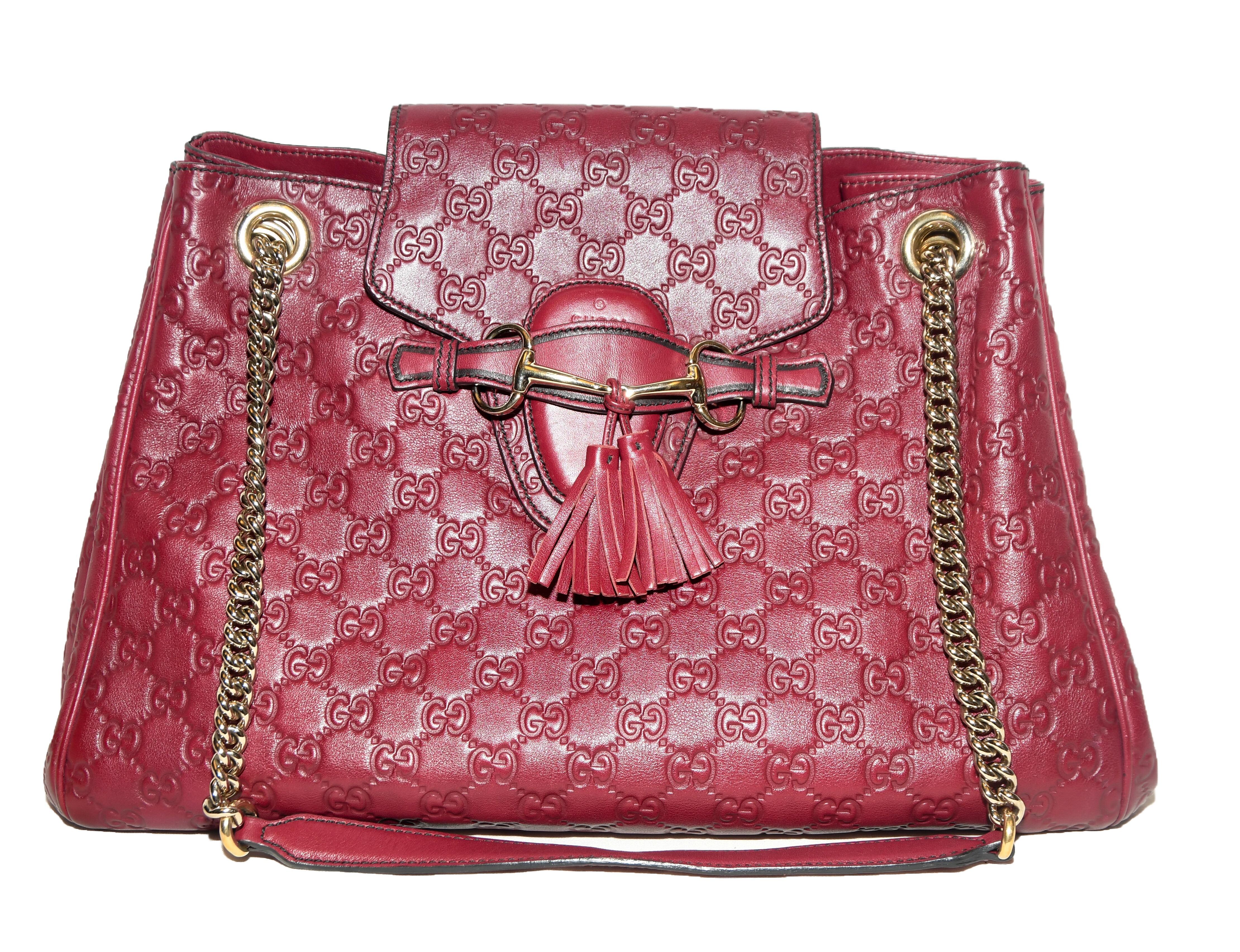 Gucci burgundy monogram embossed leather large shoulder bag includes brass tone chain link shoulder straps.  This single central pocket contains a small flap with tassel for closure at front.  The bag is lined in beige canvas.  Made in Italy 