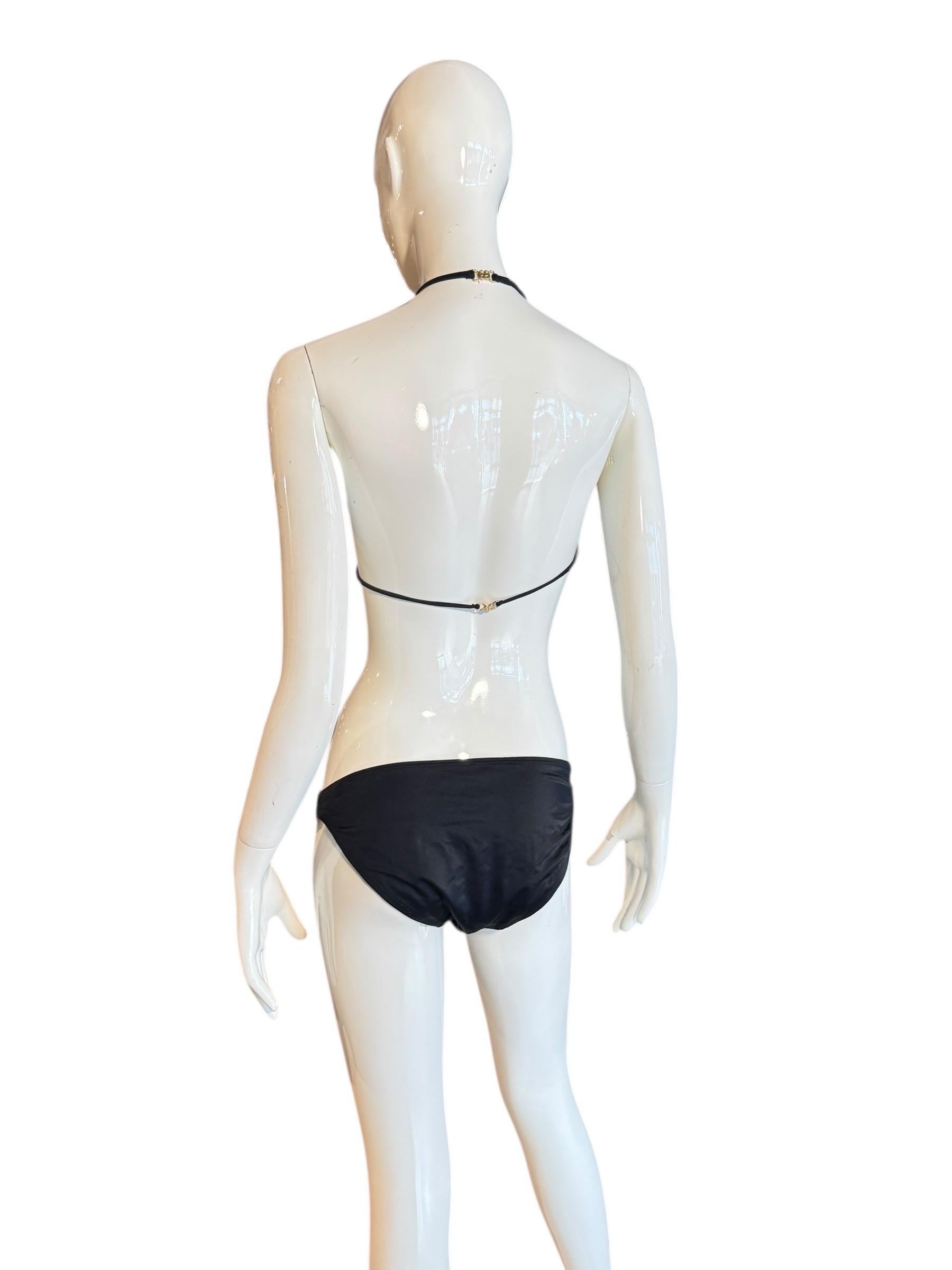 Questo bikini nero, un pezzo ultra-raro e iconico della collezione primavera/estate 2001 di Tom Ford for Gucci, è caratterizzato da un top minimalista in stile halter e da uno slip a vita bassa, impreziosito da un audace logo 