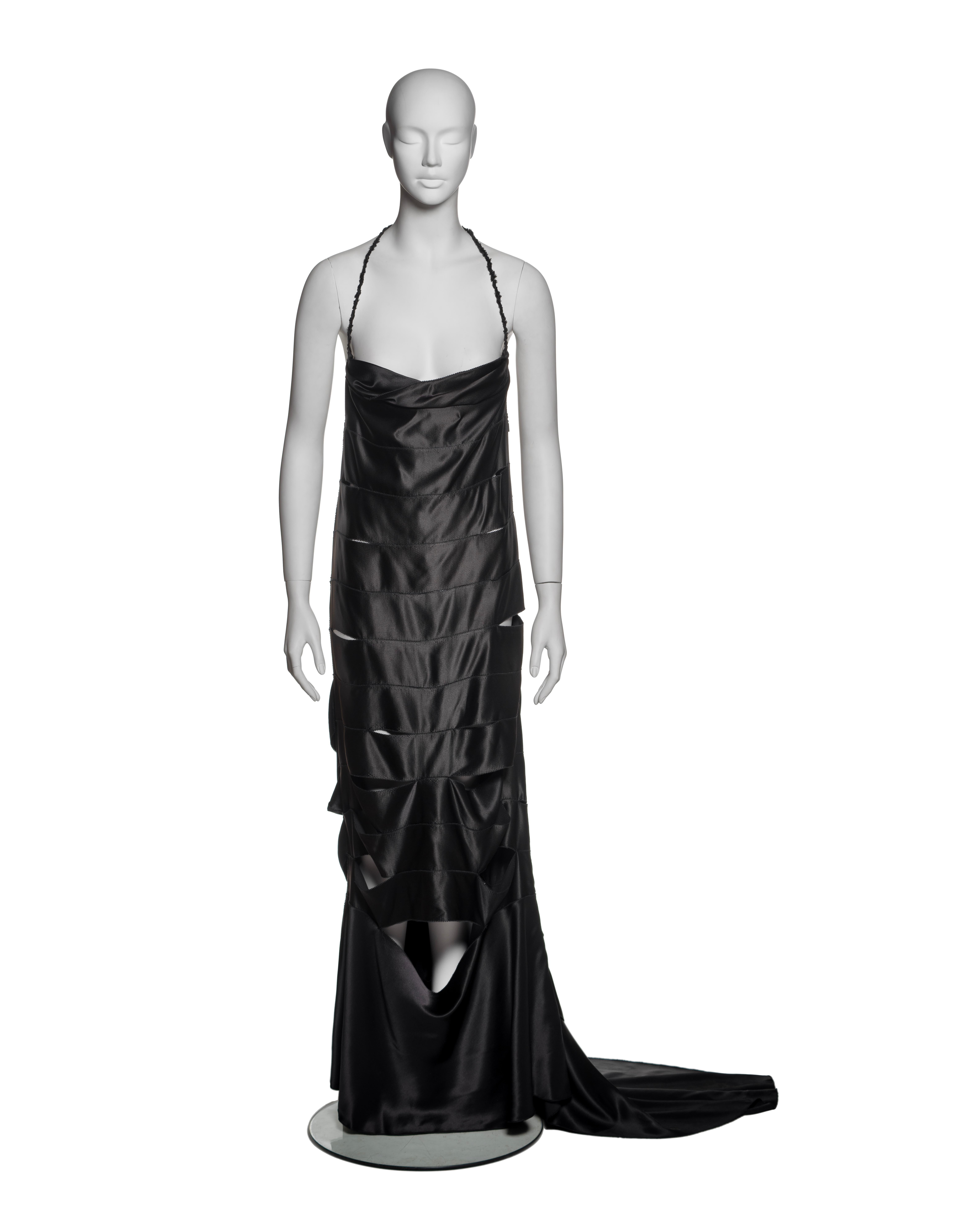 Gucci by Tom Ford, Fall-Winter 2002: A black silk evening gown with a halter neckline and a floor-length silhouette. The gown features a series of horizontal, laser-cut panels creating a layered, deconstructed effect. The cut-out detailing allows