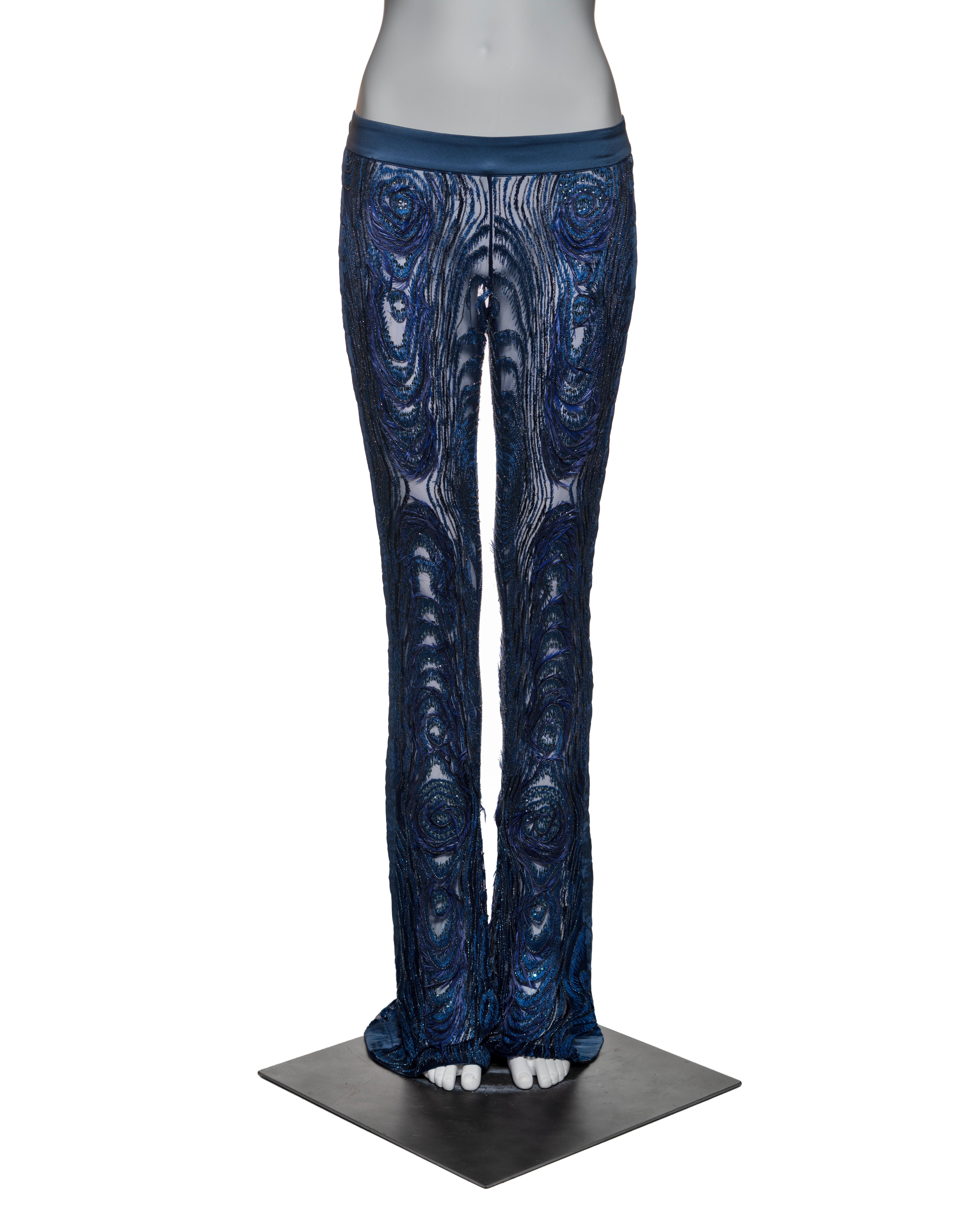 These Gucci trousers, crafted from sheer silk mesh, feature hand-embroidered peacock feather-inspired motifs in rich blues and indigo. Real feathers add luxurious texture, while pleated satin side strips and a satin waistband provide elegant