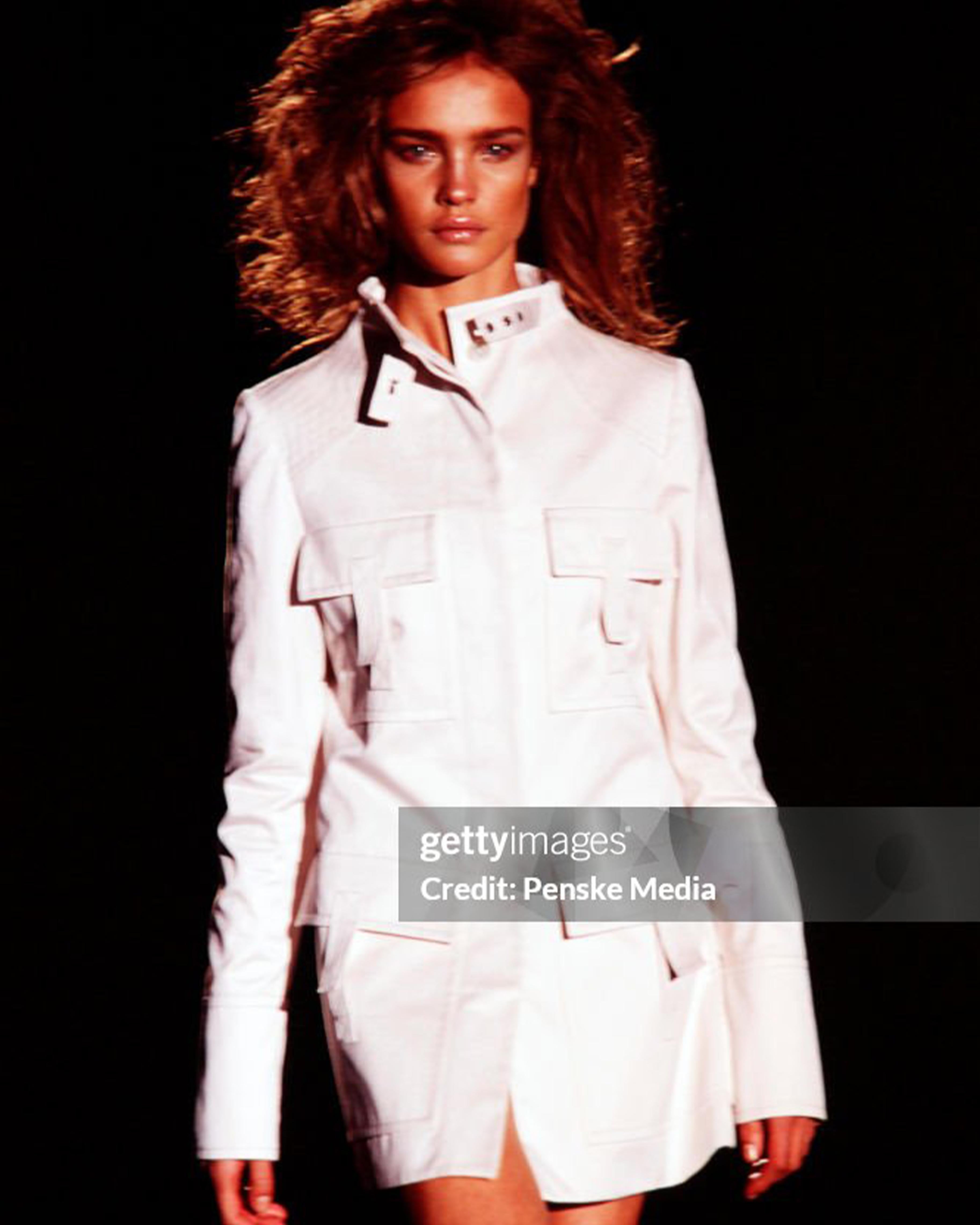 - Designed by Gucci by Tom Ford
- Spring Summer 2003 Collection
- Runway Look 1
- Multipocket White Trench Coat
- S/S 2003 collection
- Features multiple pockets
- High neck design with a tailored silhouette
- Belt closure at the neckline to adjust