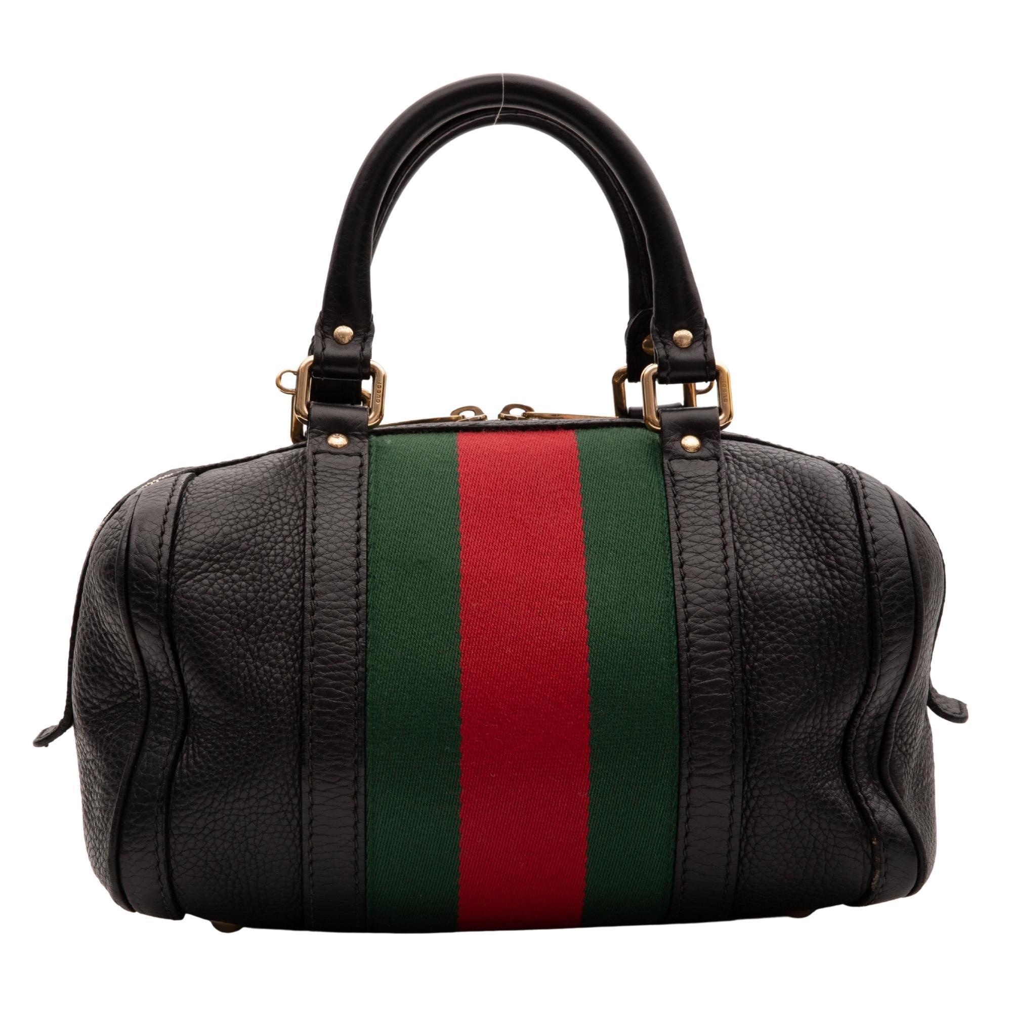 This Boston style bag is made of textured calfskin leather in black. The bag features a red and green canvas stripe around the girth of the bag, dual rolled leather top handles, brass hardware, top zip closure with double zip tabs and a beige fabric