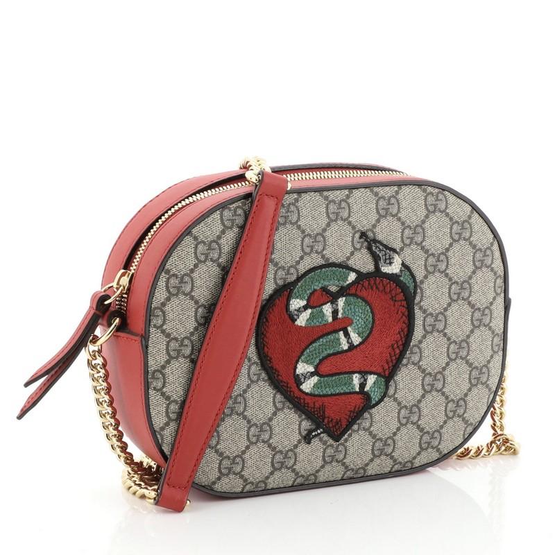 This Gucci Chain Crossbody Bag Embroidered GG Coated Canvas Mini, crafted from brown GG coated canvas and red leather, features chain link strap with leather pad, embroidered detail, and gold-tone hardware. Its zip closure opens to a neutral
