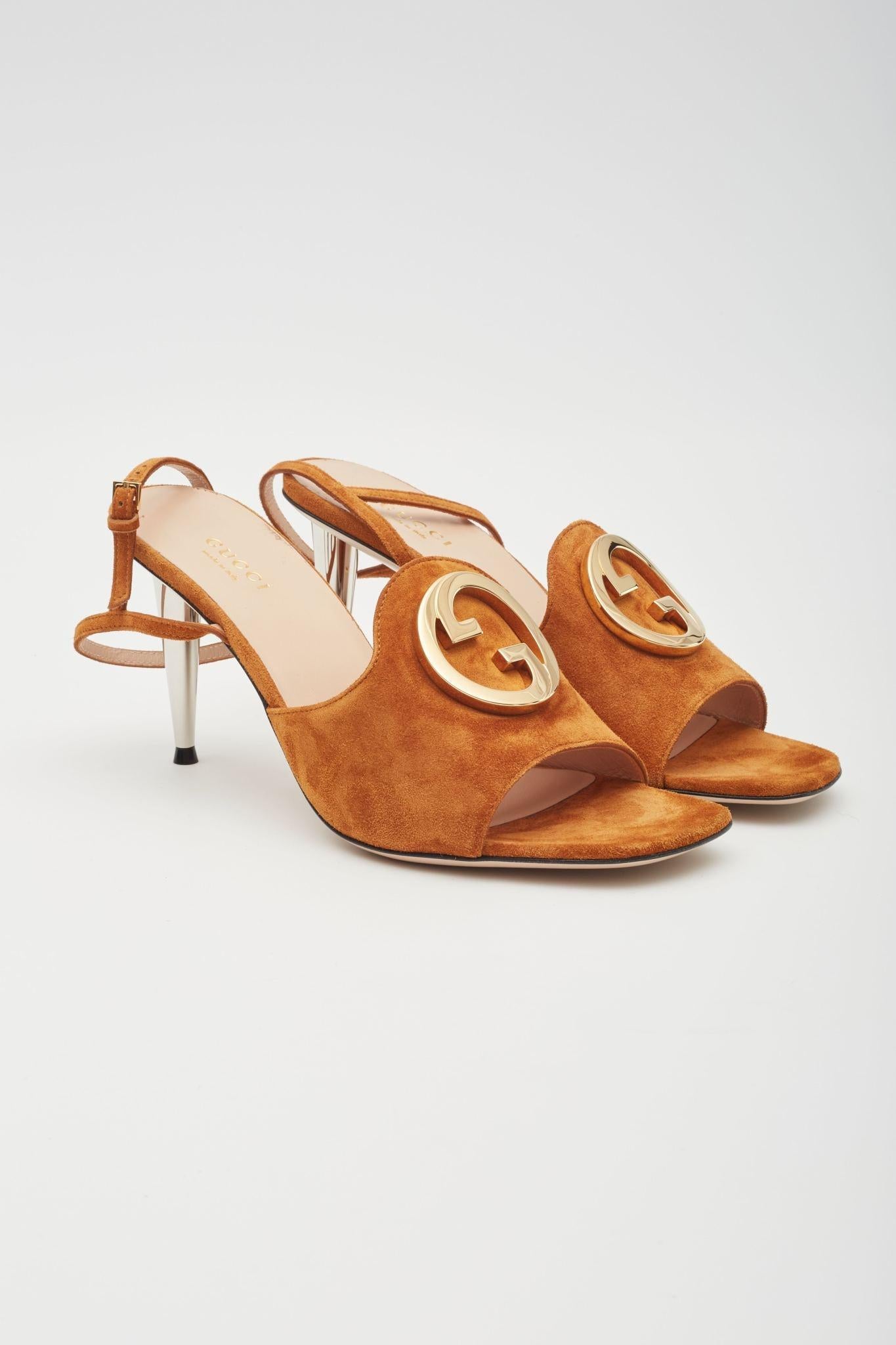 Introducing the Gucci blondie heel in congac featuring an open square toe, a buckled ankle strap, logo hardware at toe, and a 3.25