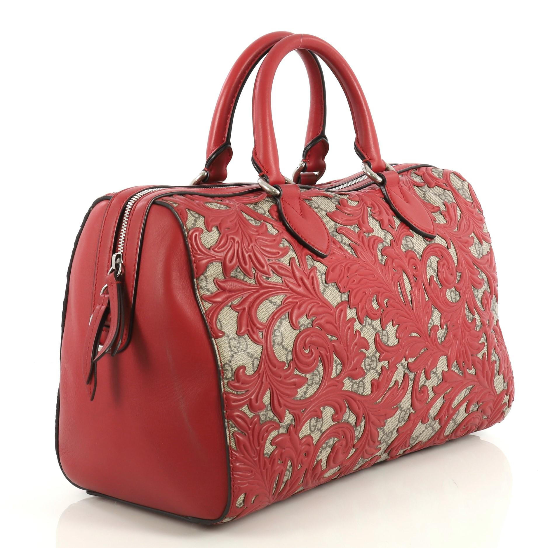 This Gucci Convertible Boston Bag Arabesque GG Coated Canvas Medium, crafted from brown GG supreme coated canvas with an overlay of red leather floral Arabesque pattern, features dual rolled leather handles and silver-tone hardware. Its zip closure