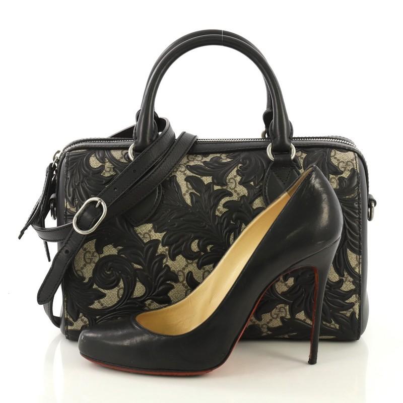 This Gucci Convertible Boston Bag Arabesque GG Coated Canvas Small, crafted from brown arabesque GG coated canvas and black leather, features dual rolled leather handles, overlay of black leather floral arabesque pattern, and aged silver-tone
