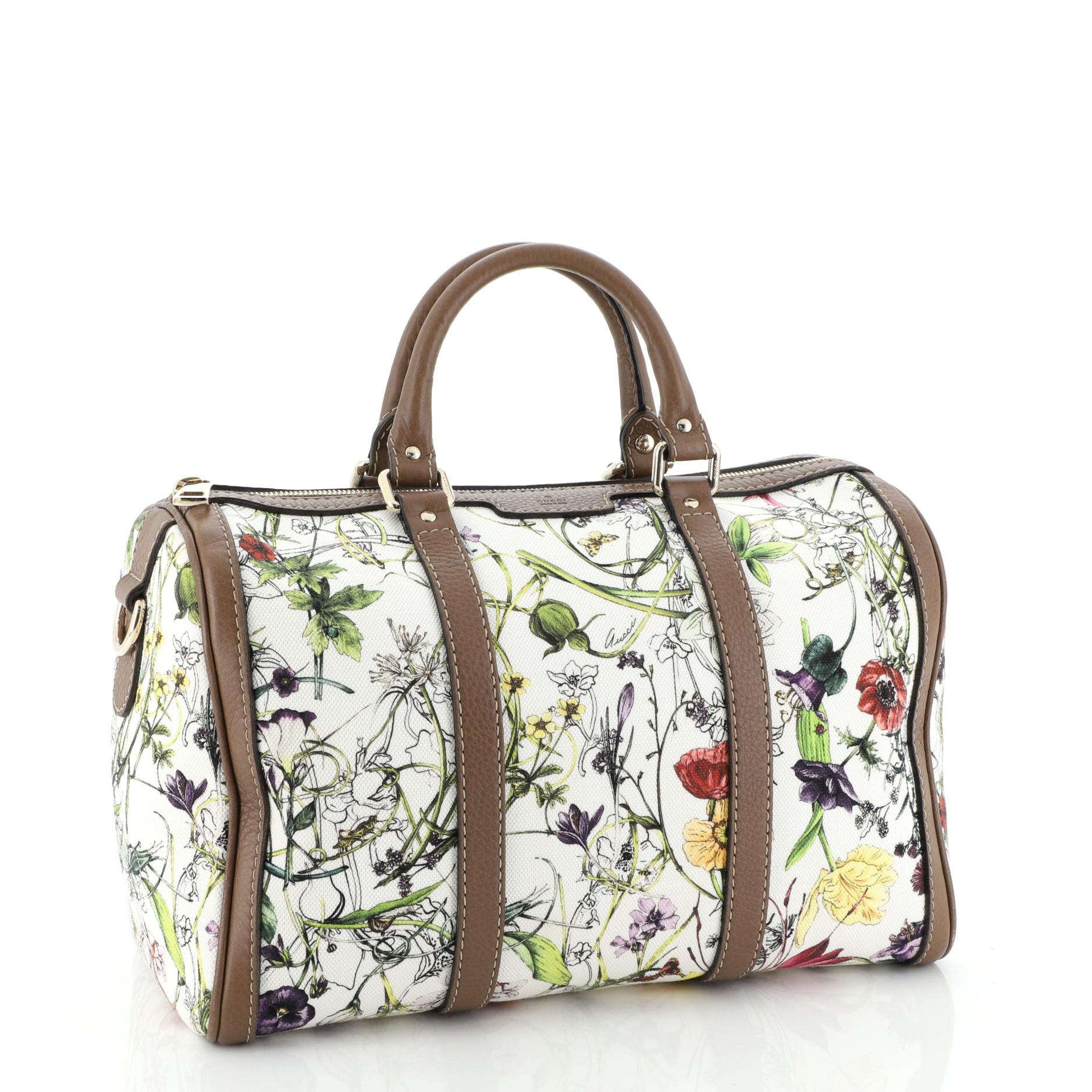 This Gucci Convertible Joy Boston Bag Flora Canvas Medium, crafted in white canvas with flora print overlay, features dual rolled leather handles, leather trim, and gold-tone hardware. Its zip closure opens to a neutral canvas interior with side zip