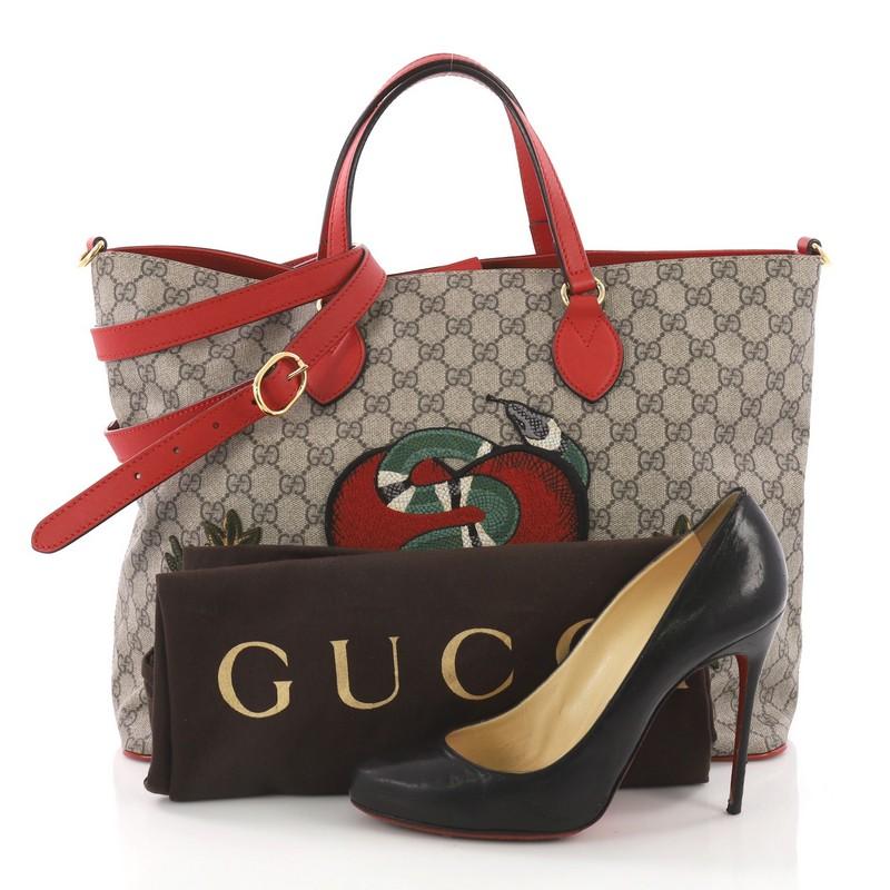 This Gucci Convertible Soft Tote Embroidered GG Coated Canvas Medium, crafted in brown embroidered coated canvas, features dual flat leather handles, red leather trims, and gold-tone hardware. Its hidden magnetic closure opens to a blush microfiber