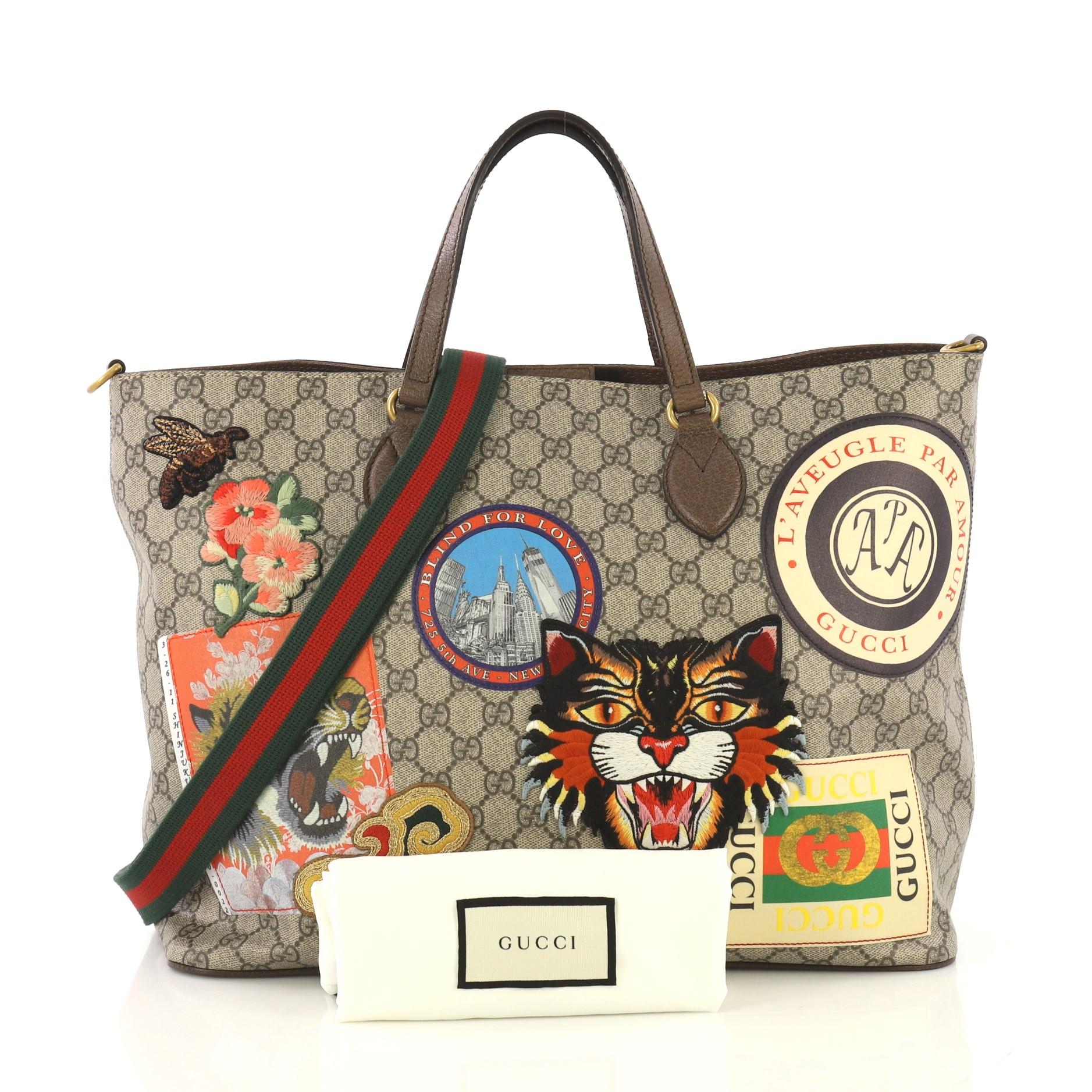 This Gucci Courrier Convertible Soft Open Tote GG Coated Canvas with Applique Large, crafted in beige GG coated canvas, features dual flat leather handles, embroidered appliqués of angry cat, clouds, bee and vintage Gucci logo, and aged gold-tone