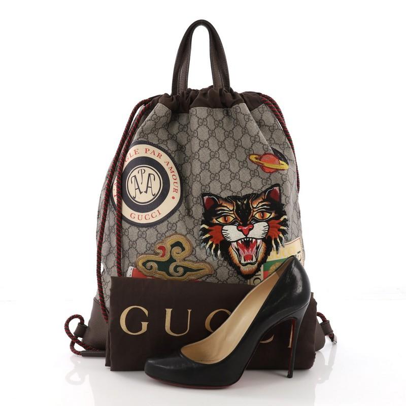 This Gucci Courrier Soft Drawstring Backpack GG Coated Canvas with Applique Medium, crafted in brown GG coated canvas, features applique design, dual flat leather handles, rope straps that double function as a drawstring, and brass-tone hardware.
