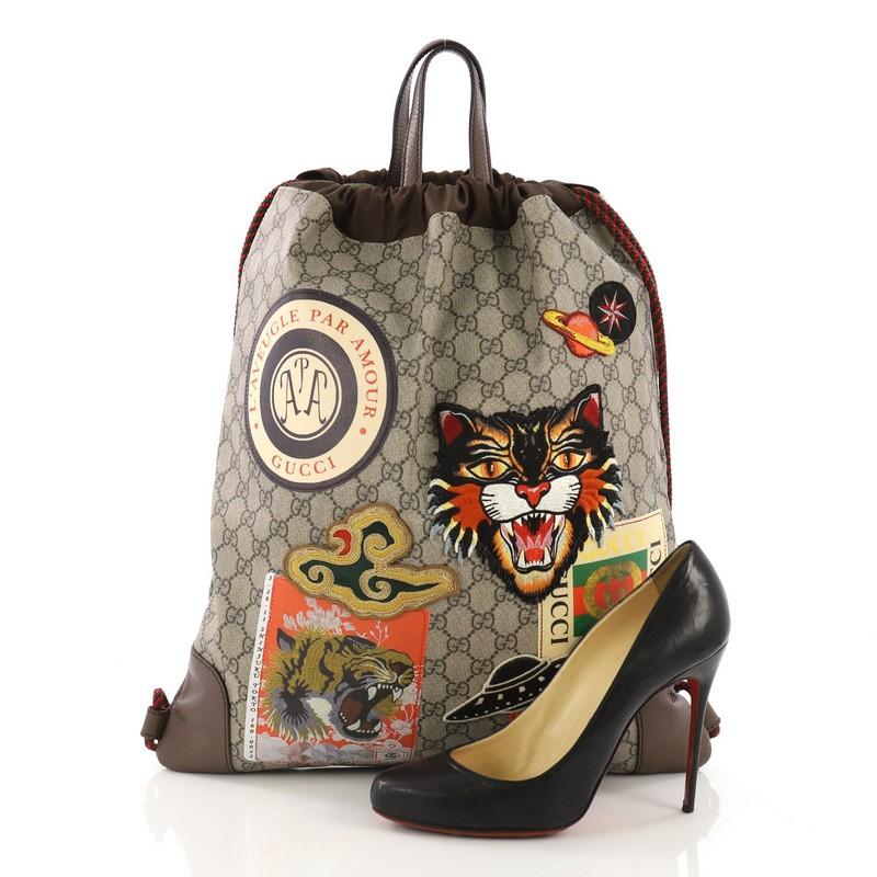 This Gucci Courrier Soft Drawstring Backpack GG Coated Canvas with Applique Medium, crafted in brown GG coated canvas, features applique design, dual flat leather handles, rope straps that double function as drawstring, and aged gold-tone hardware.