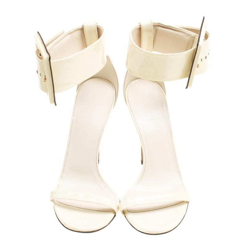 These Gucci sandals are artfully crafted in cream-colored patent leather that lends it a contemporary chic look. Featuring an open toe silhouette, this pair comes with an ankle strap and secured with chunky buckle closure in matching hue. Look