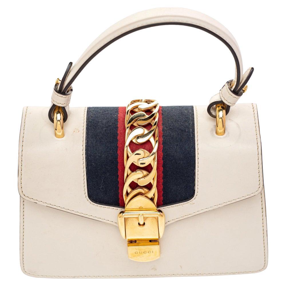 From the house of Gucci comes this gorgeous Sylvie bag that will perfectly complement all your outfits. It has been luxuriously crafted from cream leather and styled with a chain-web decorated flap and a buckle lock to secure the suede interior. The