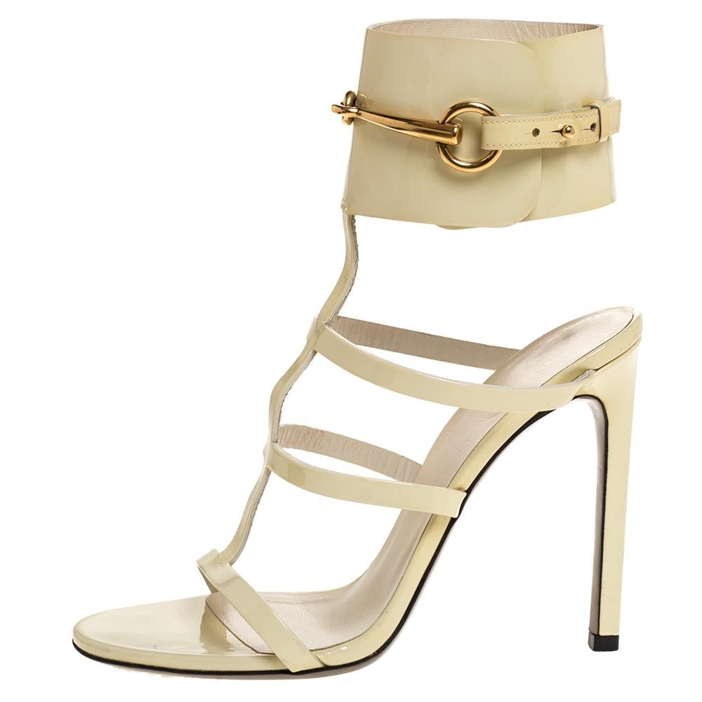 These Ursula gladiator sandals by Gucci are stylish, minimalistic, and sleek. Made from cream-colored patent leather, they are adorned with straps across their fronts and thick adjustable ankle straps with Gucci horsebit detailing. They have open