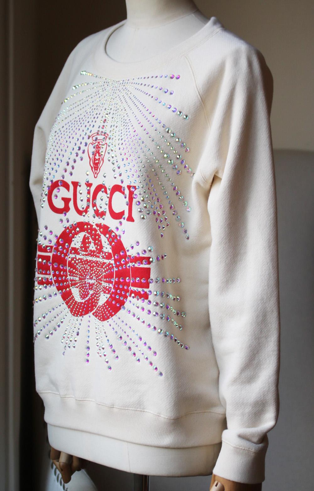 Ivory cotton sweatshirt from luxury brand Gucci, with a sparkly crystal appliqué and red interlocking 'G' logo print. It is made in mid-weight jersey, with a ribbed collar, cuffs and hem. Crystal detail. 100% Cotton. Made in Italy. 

Size: Medium