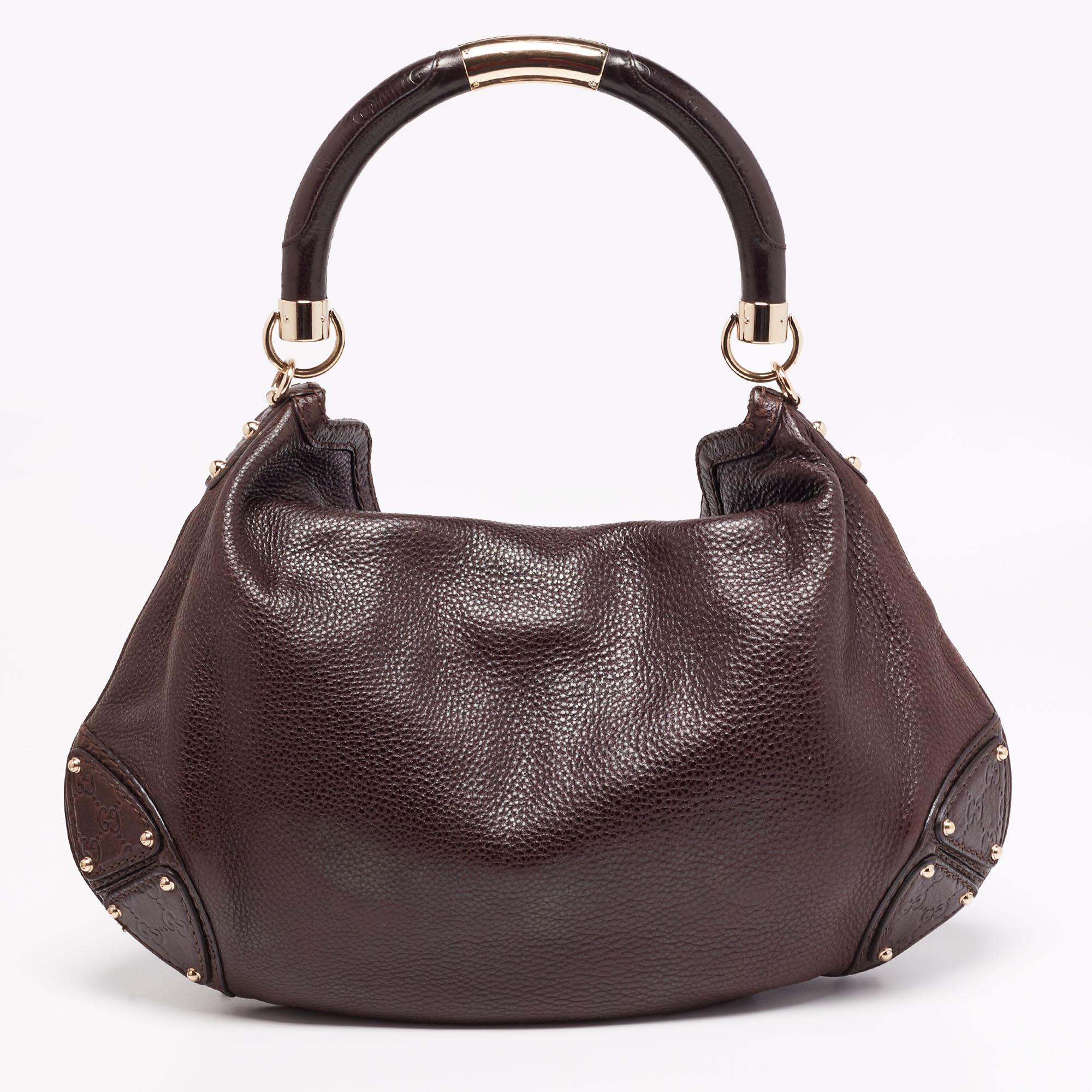 The Gucci Babouska Indy is a modern everyday bag with a chic Bohemian finish. This dark brown bag is made of leather that is adorned with double tassels having Bamboo details. It is finished with studs, an engraved top handle, and a shoulder strap.