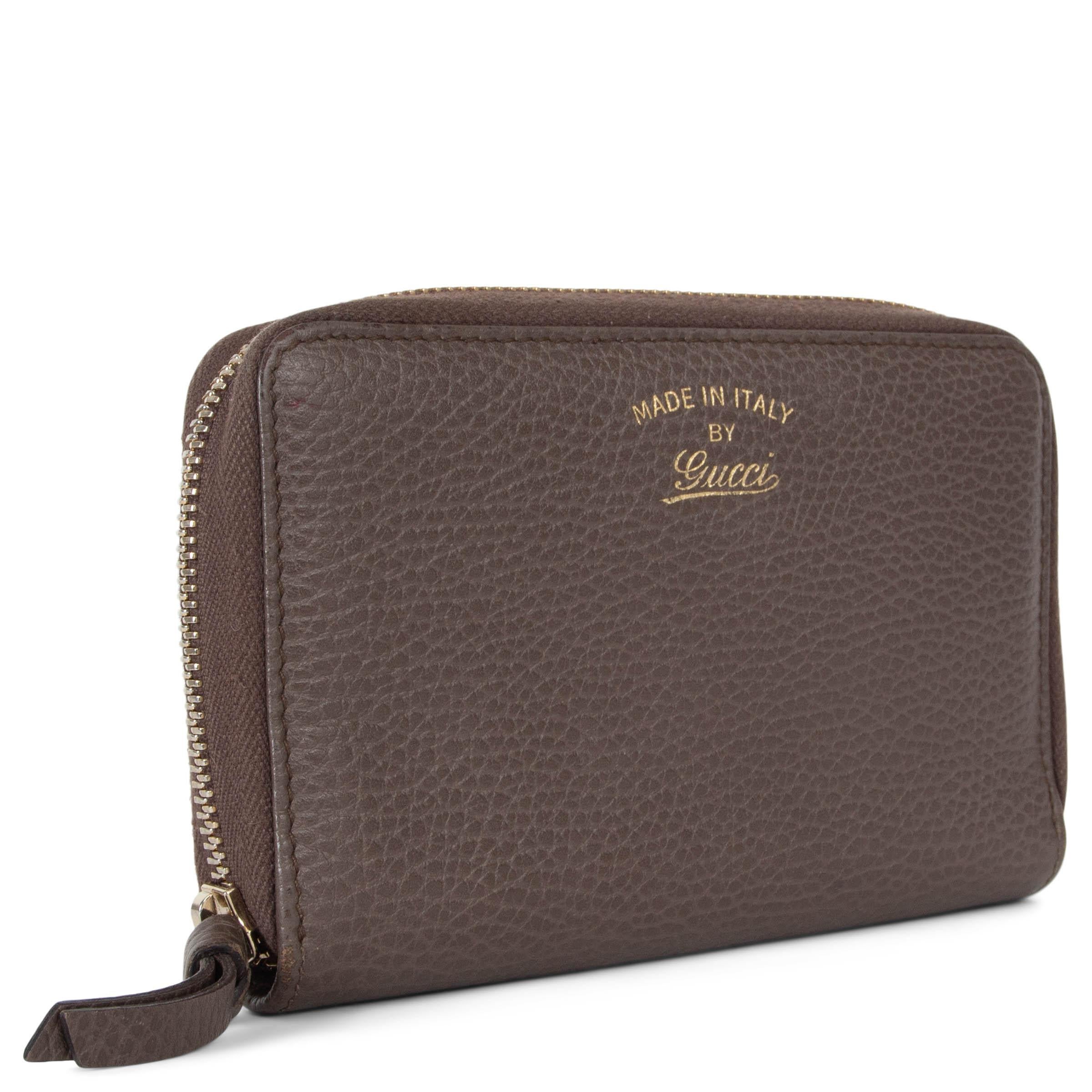 This 100% authentic Gucci Swing wallet in taupe grained leather combines functionality with understated luxury. Featuring a gold embossed logo on the front, it opens with a zipper to reveal a leather-lined interior. The wallet is thoughtfully
