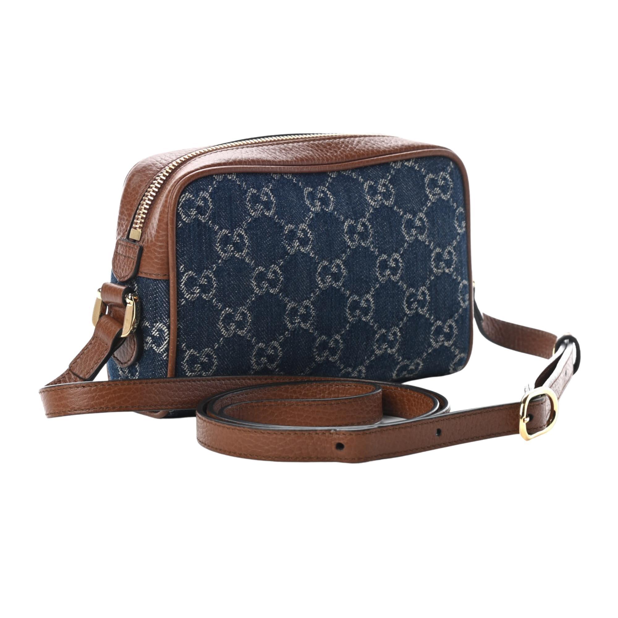 This camera-style bag is made of monogram GG jacquard dark blue denim with a soft construction. The bag features an enamelled GG logo detail, brown leather trim, gold-toned hardware, an attached key ring, a front zipper pocket, top zip closure, an