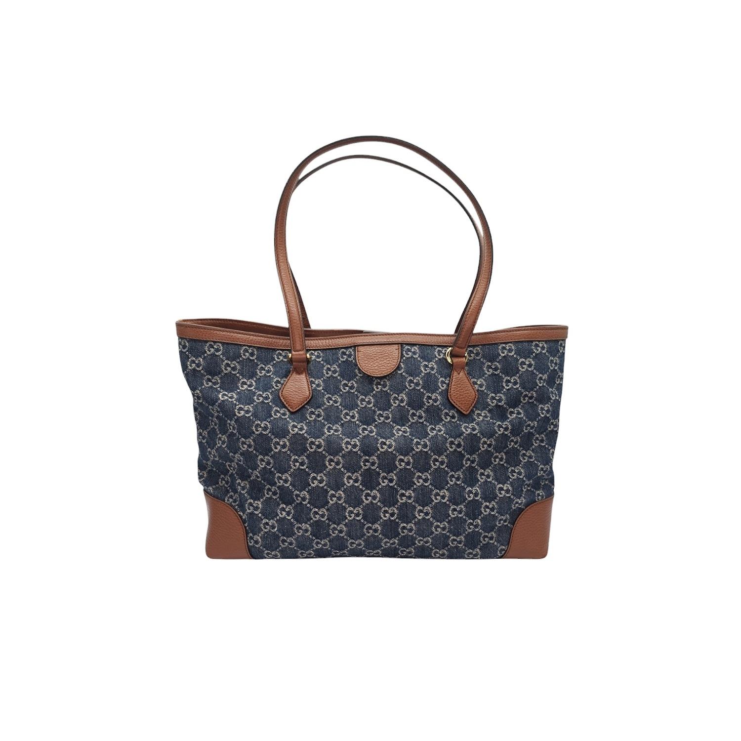 This Gucci Denim GG Monogram Medium Ophidia Shopping Tote is crafted of Gucci GG monogram denim. The handbag features brown leather strap handles and the top is open to a beige fabric interior with zipper and patch pockets.

Designer: