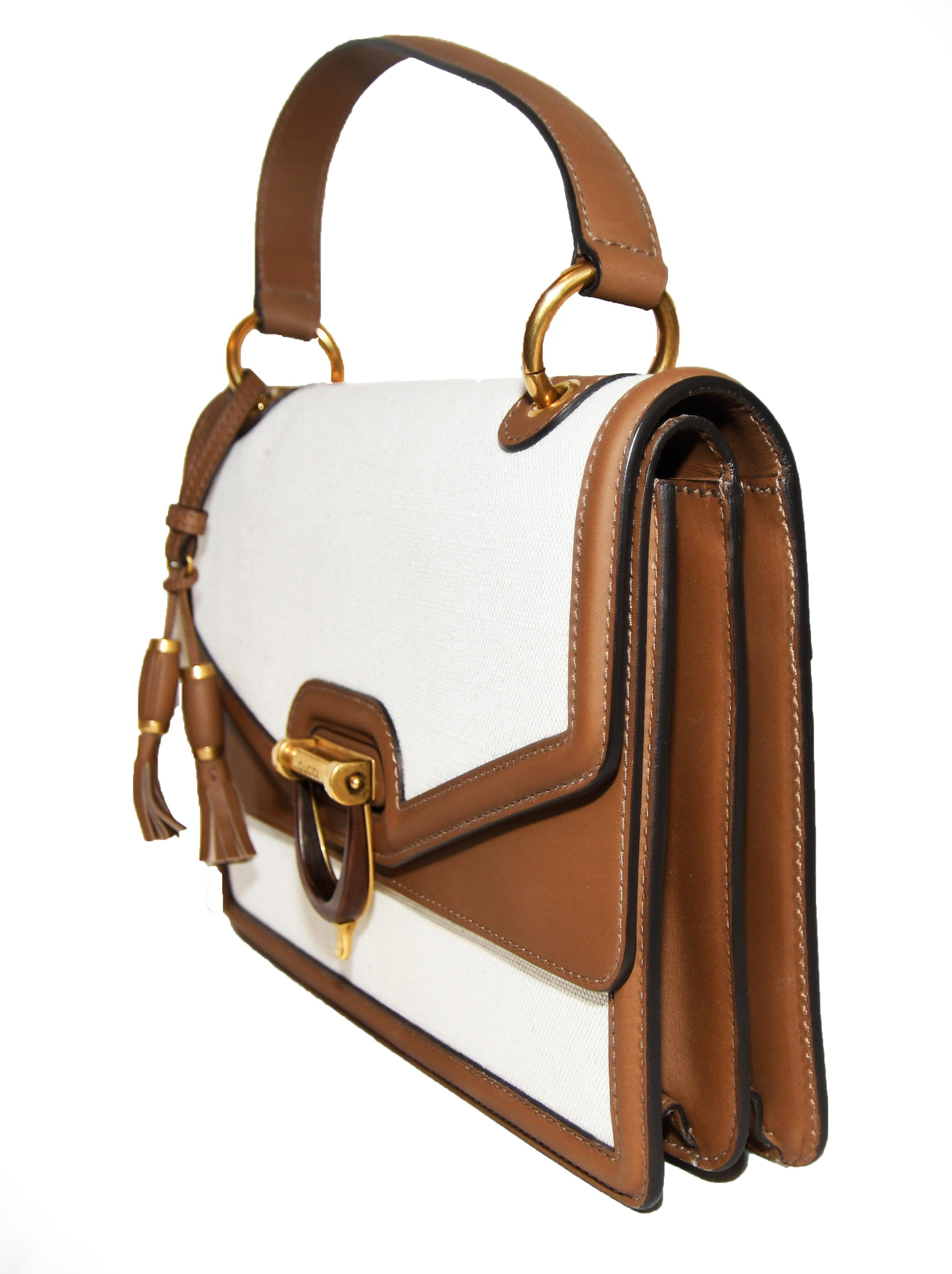 Gucci Derby canvas in beige and trimmed in brown leather bag has one brown leather top handle with decorative tassel on handle ring.  This double flap bag includes a horse bit turn down closure at front.  All the hardware is a semi matte gold tone. 