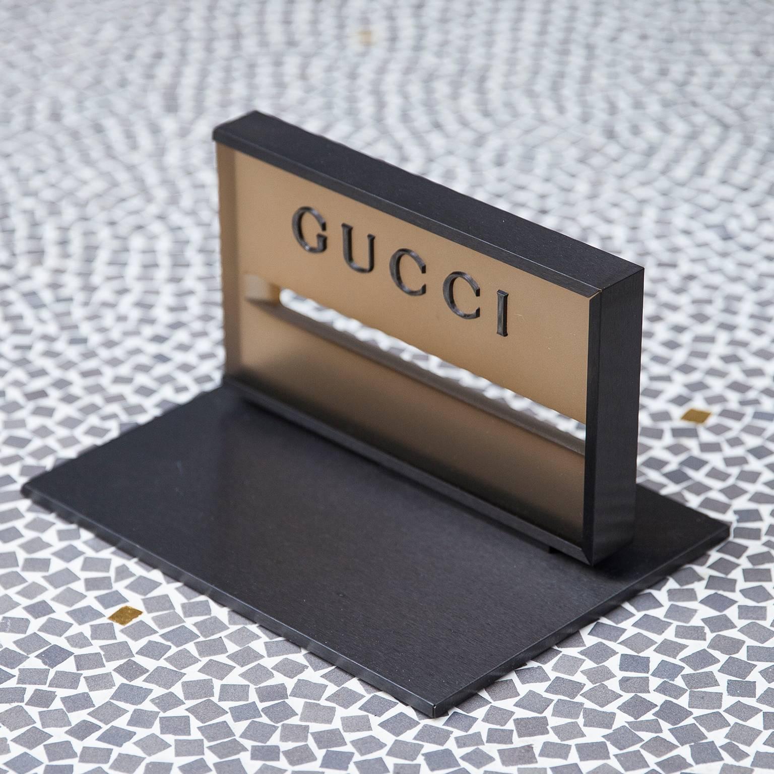 Dieser elegante Gucci-Briefbeschwerer aus den 1980er Jahren besteht aus einem anthrazitfarbenen Metallsockel und einem Acrylständer und wird Tom Ford zugeschrieben.