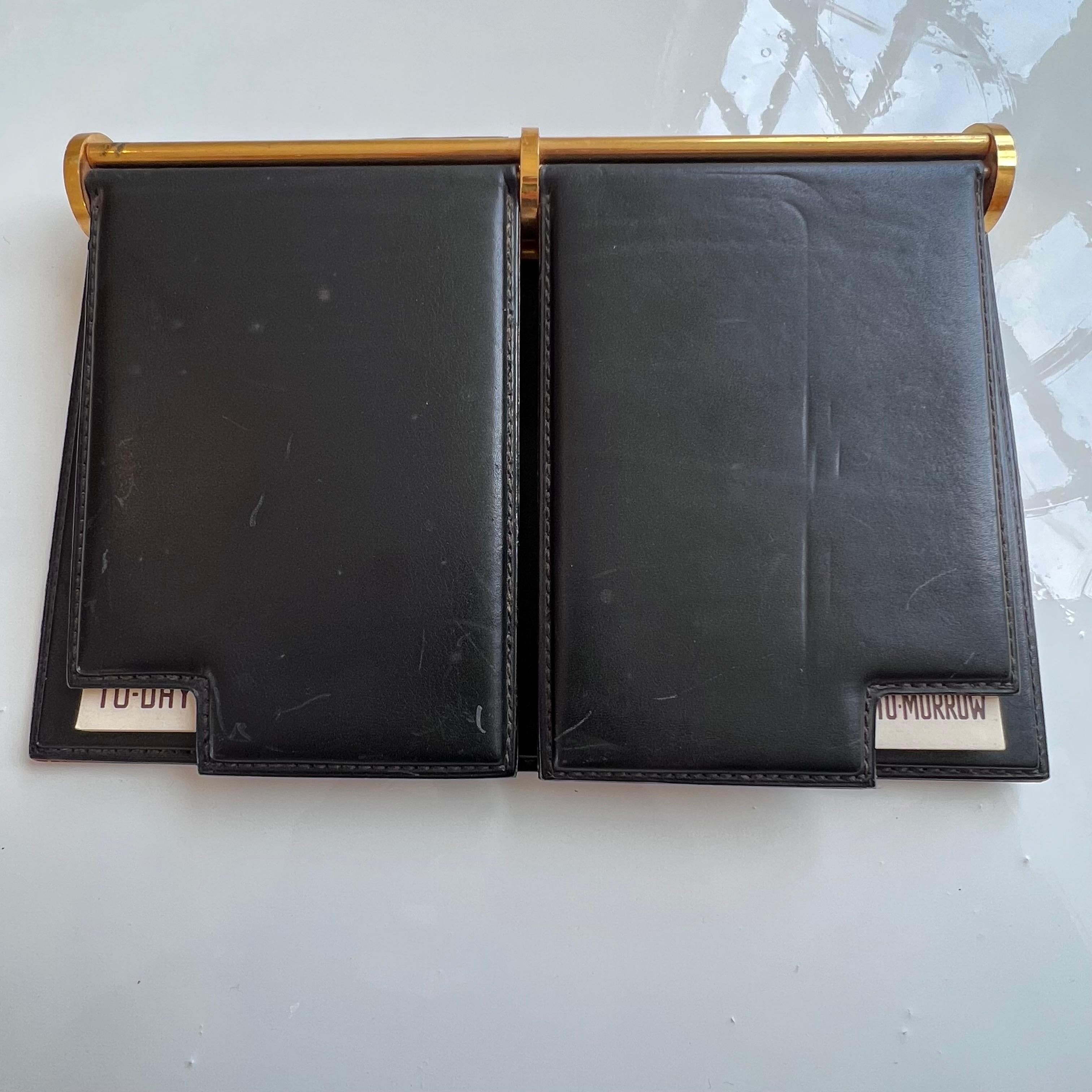 Chic black leather Gucci desk planner with brass bindings containing two notepads titled “To-day” and “To-Morrow”.  Small window at the bottom of each leather flap showing the day. Stamped “Made in Italy by Gucci” on the underside. Wonderful