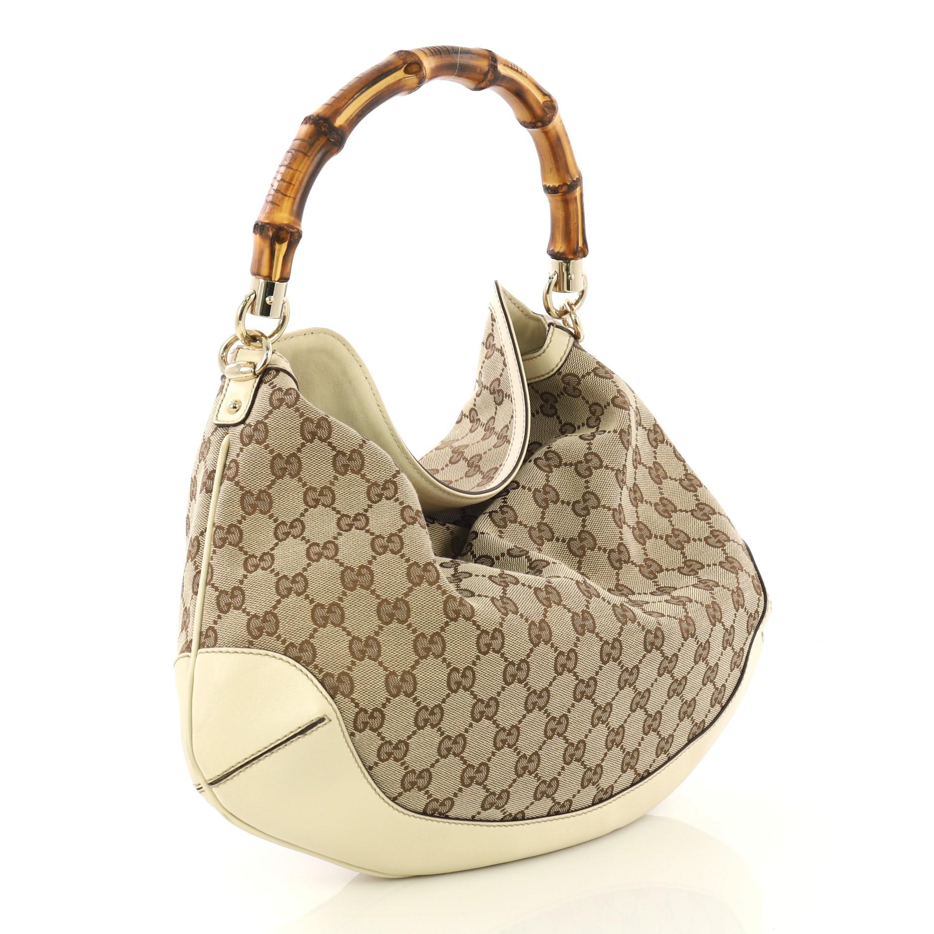This Gucci Diana Bamboo Shoulder Bag GG Canvas Medium, crafted from beige GG canvas and cream leather, features bamboo loop handle, leather base, and gold-tone hardware. Its wide top opening showcases a brown fabric interior with side zip and slip