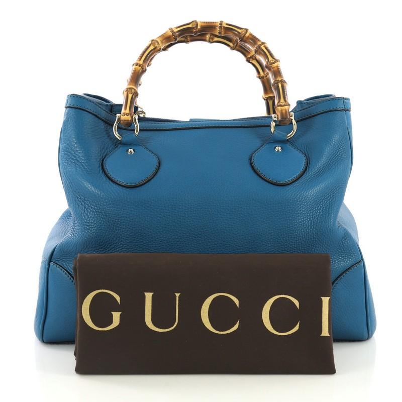 This Gucci Diana Bamboo Top Handle Tote Leather Medium, crafted from blue leather, features dual bamboo top handles, protective base studs, and gold-tone hardware. Its magnetic snap closure opens to a beige canvas interior with middle zip