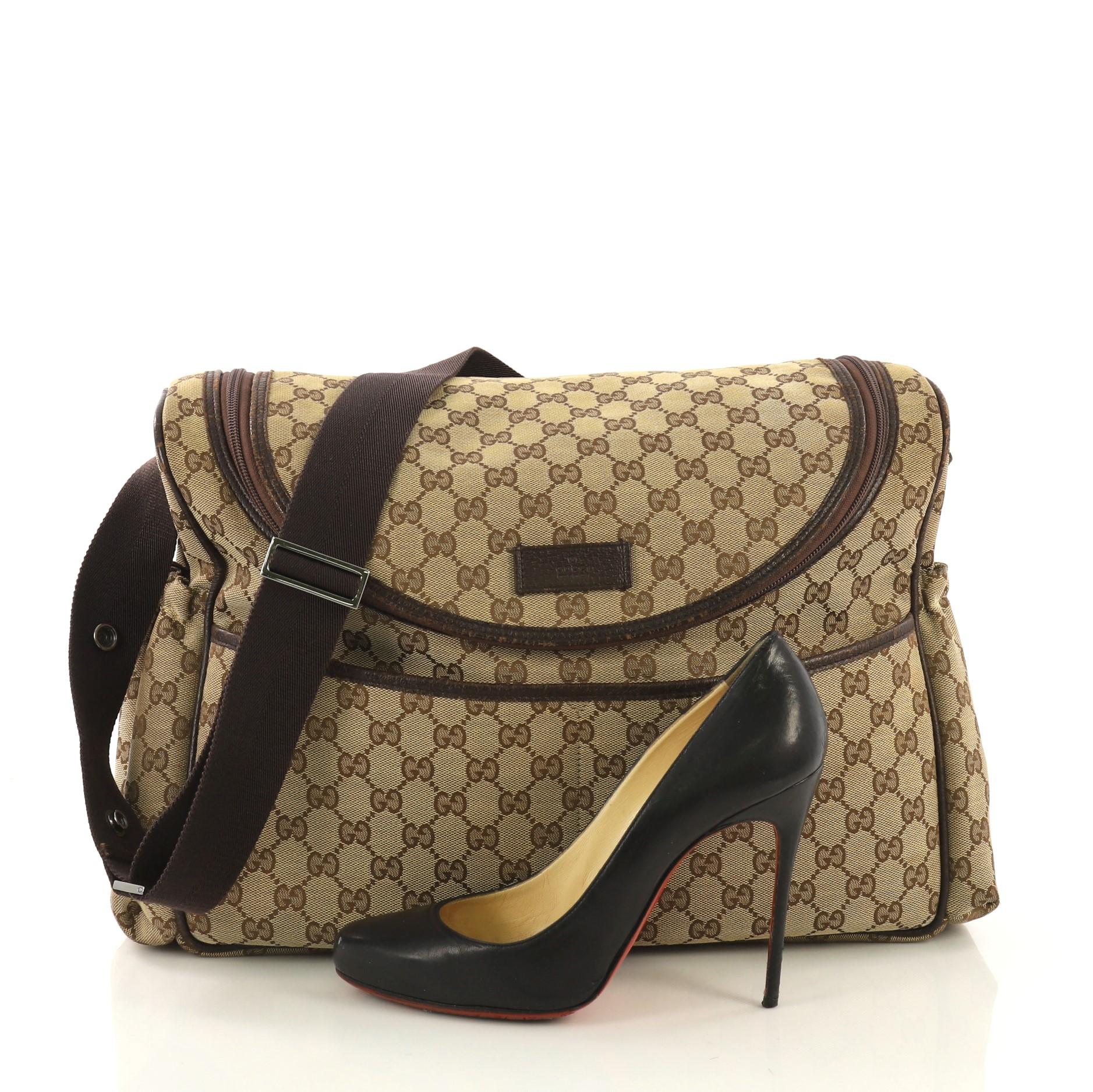 This Gucci Diaper Crossbody Bag GG Canvas, crafted from brown GG canvas, features adjustable shoulder strap, side elastic pockets, two front pockets, leather trim, and gunmetal-tone hardware. Its top zip closure opens to a brown nylon interior with