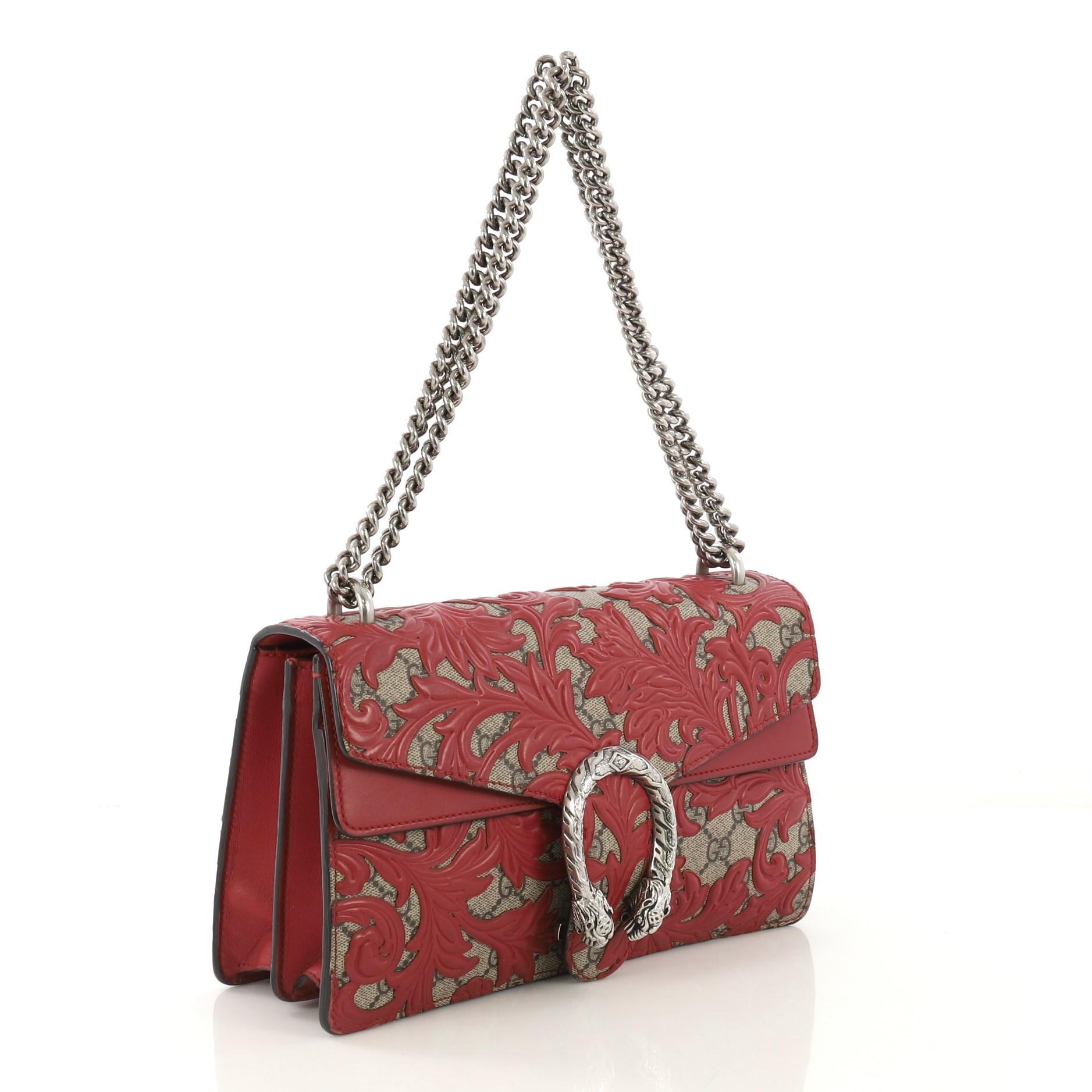 This Gucci Dionysus Bag Arabesque GG Coated Canvas Small, crafted from brown GG monogram coated canvas and red leather, features a chain link strap, embellished tiger head spur detail on its flap, accordion-like gusseted sides, and aged silver-tone